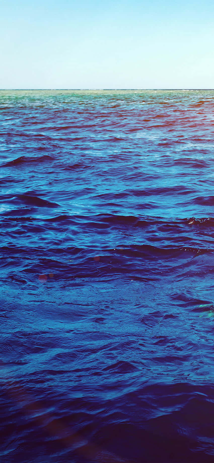 Ocean Aesthetic Phone 桌布 壁紙 — 廣闊的海洋波浪在清澈的天空下泛起漣漪，帶有漸變的藍色和紫色色調。