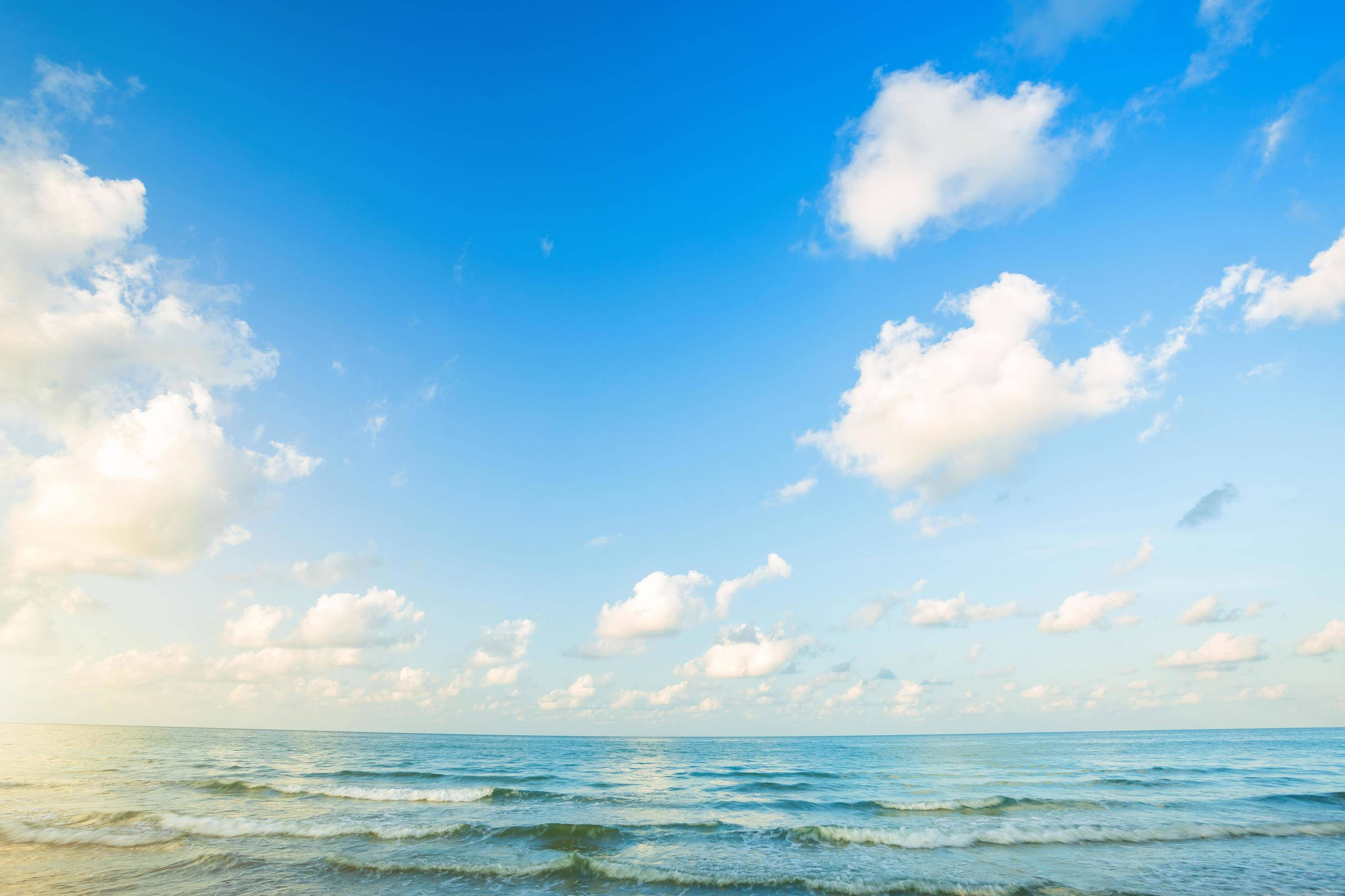 海洋 桌布 壁紙 — 廣闊的海洋波浪在金色時刻，於點綴著蓬鬆白雲的明亮藍天下翻滾。
