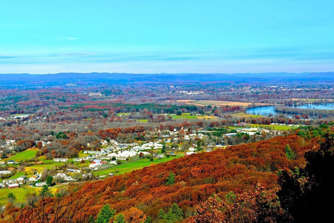 Massachusetts 桌布 壁紙 — 廣闊的秋景展現出一個山谷，覆蓋著火紅和橙色的樹葉，散落的白色房屋坐落在連綿起伏的丘陵之間，在清澈的藍天下。
