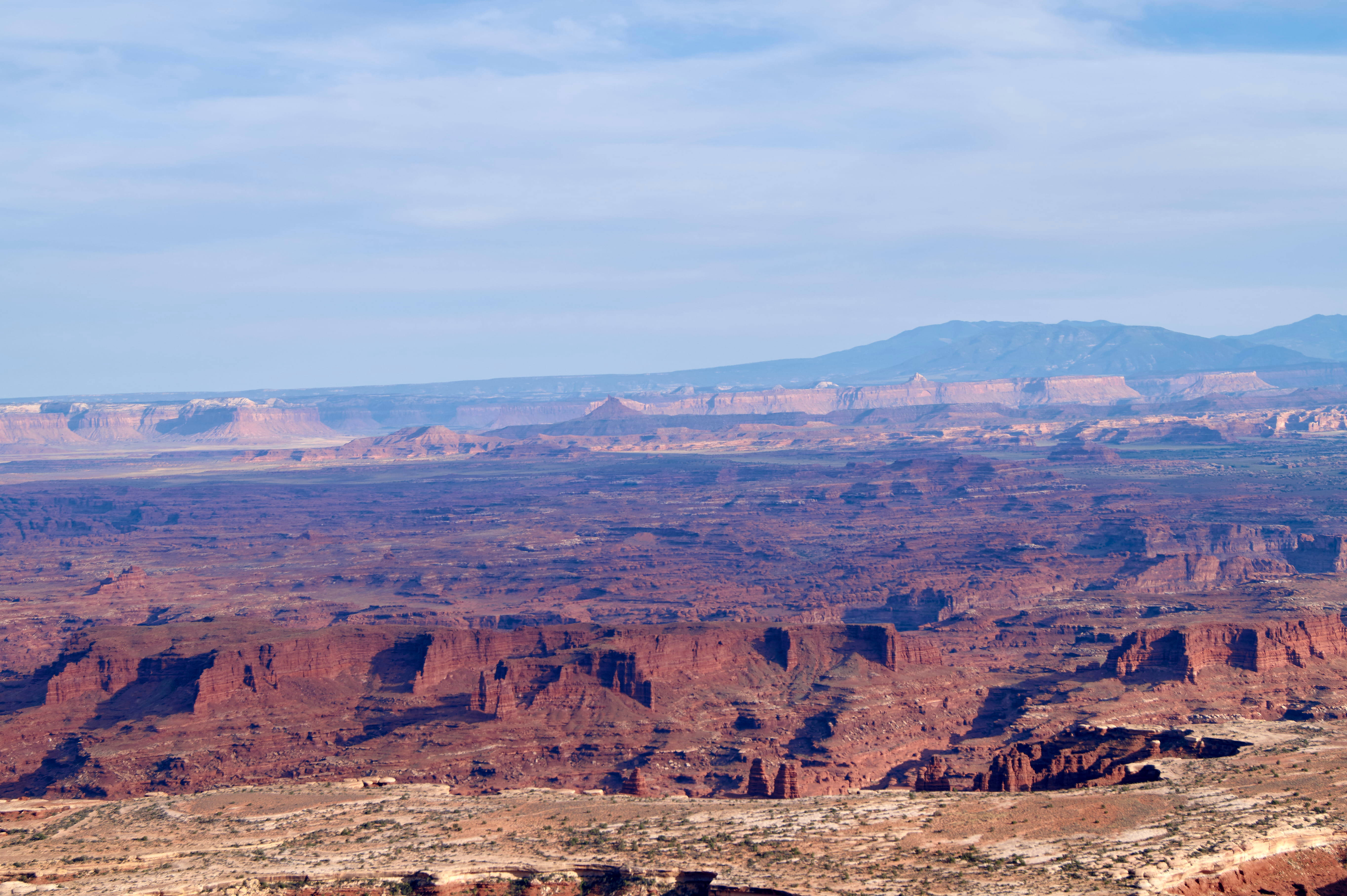 Canyonlands National Park 桌布 壁紙 — 廣闊的紅色岩石峽谷在淡藍色天空下延伸，遠處的平頂山逐漸消失在朦朧的地平線中。