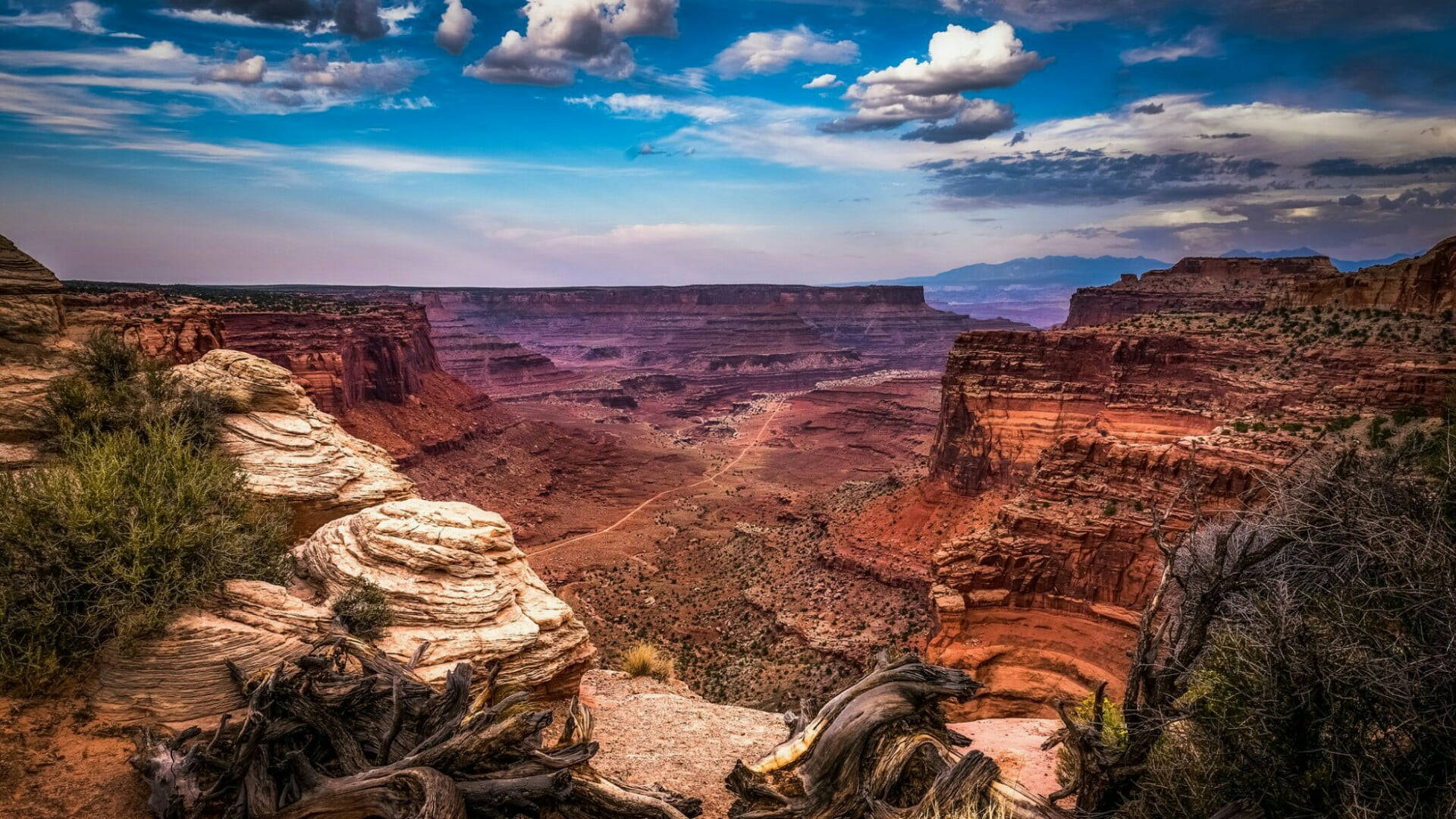 Canyonlands National Park 桌布 壁紙 — 廣闊的紅色峽谷在戲劇性的藍天下延伸，有蓬鬆的白雲和蜿蜒的土路。