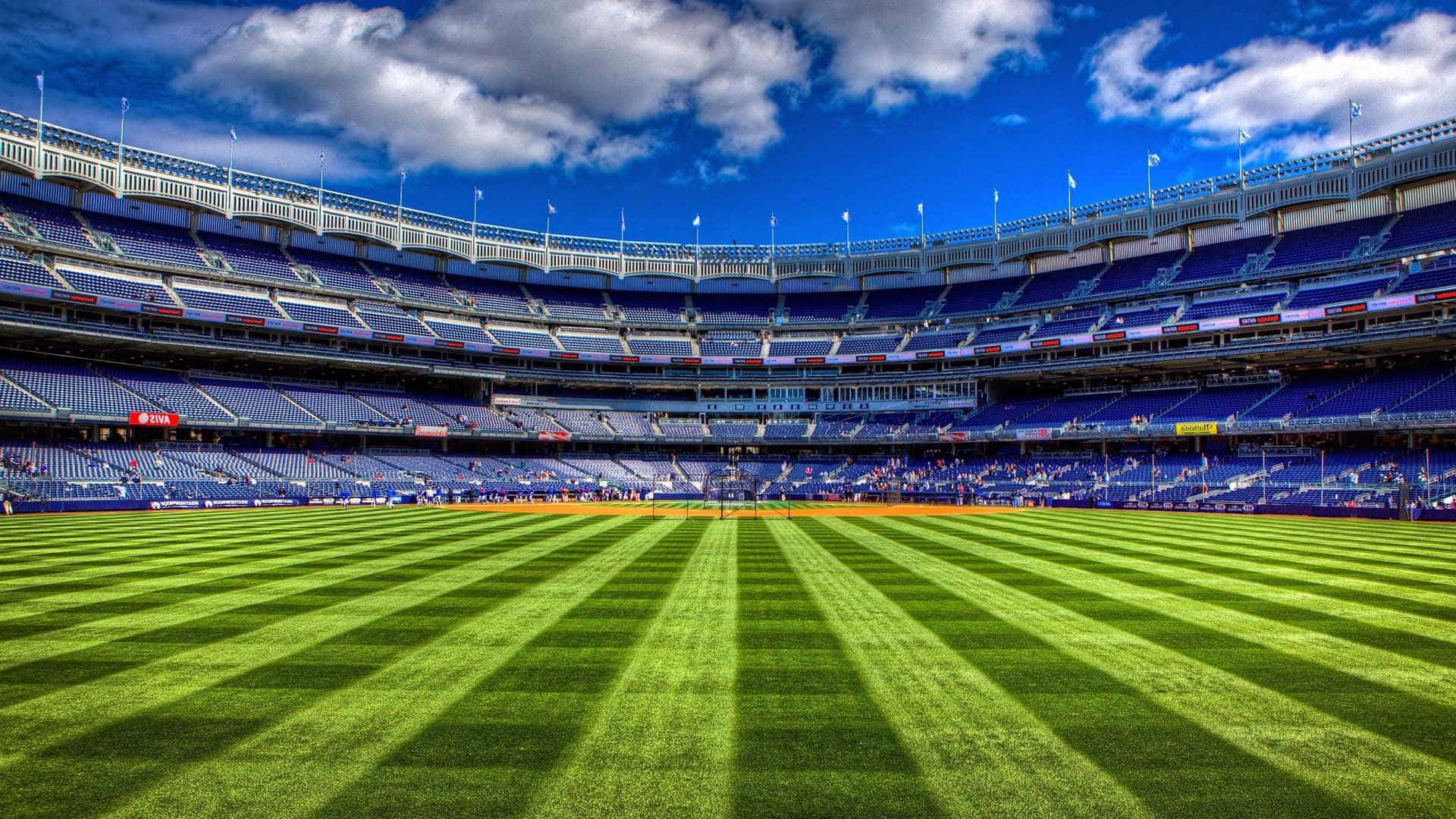 Football Field 桌布 壁紙 — 廣闊的綠色棒球場，在明亮的藍天白雲下，有藍色的空座位。
