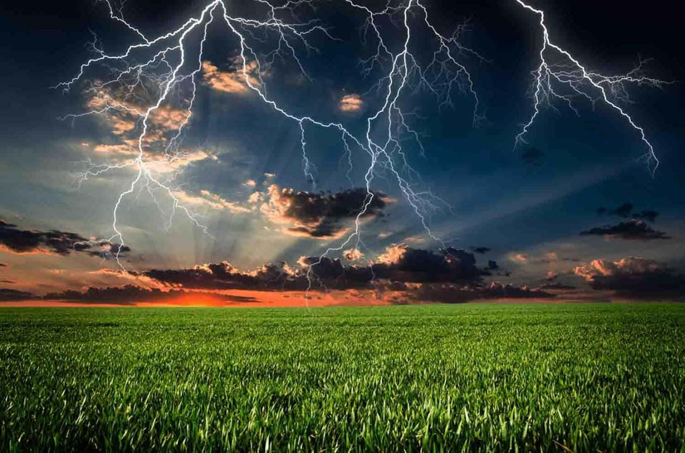 Thunderstorm 桌布 壁紙 — 廣闊的綠色田野在戲劇性的天空下延伸，多道閃電在日落地平線上劈啪作響。