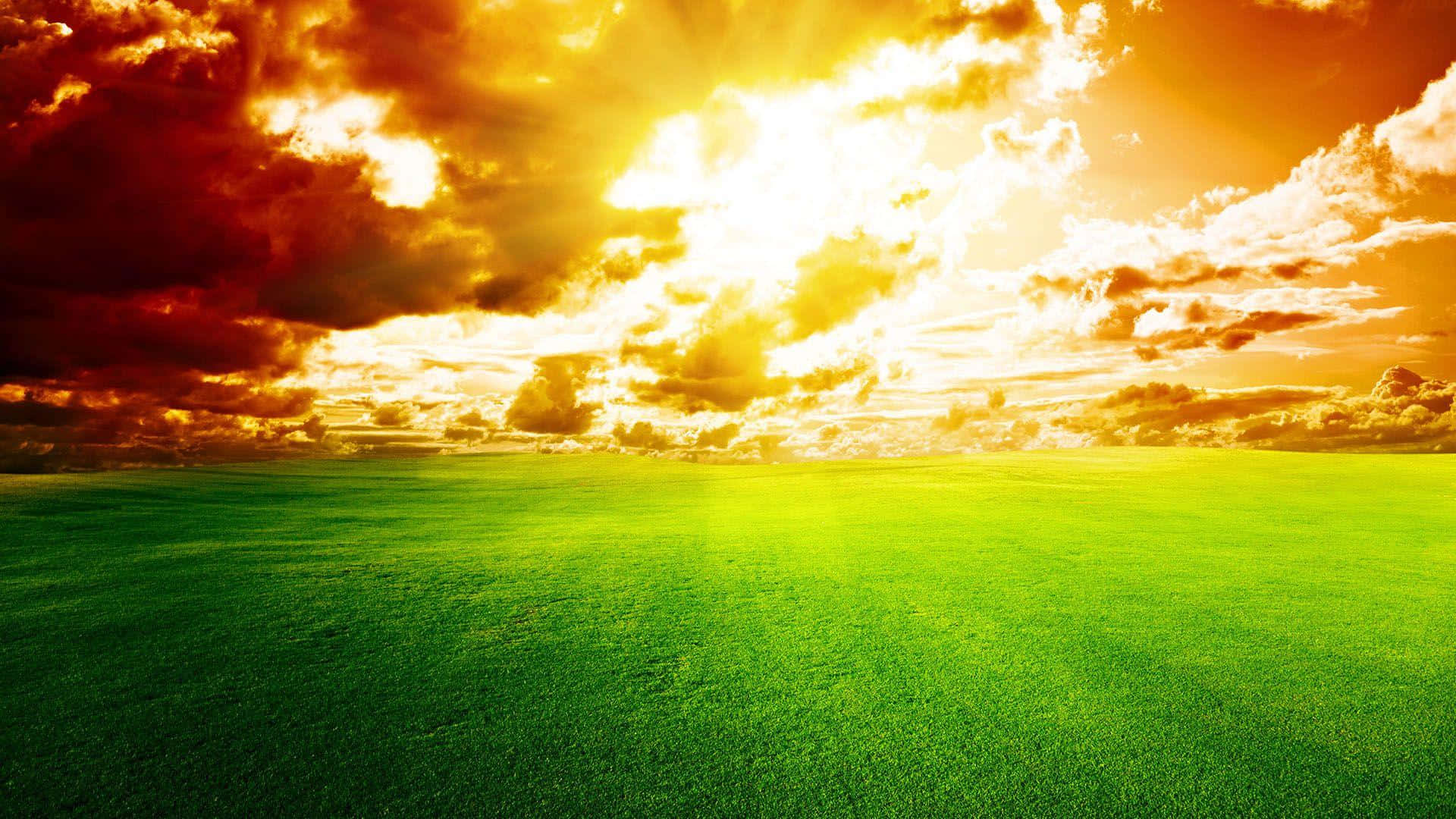 Sky Clouds 桌布 壁紙 — 廣闊的綠色田野在戲劇性的日落天空下延伸，天空中有火紅的橙色雲彩和燦爛的金色陽光。