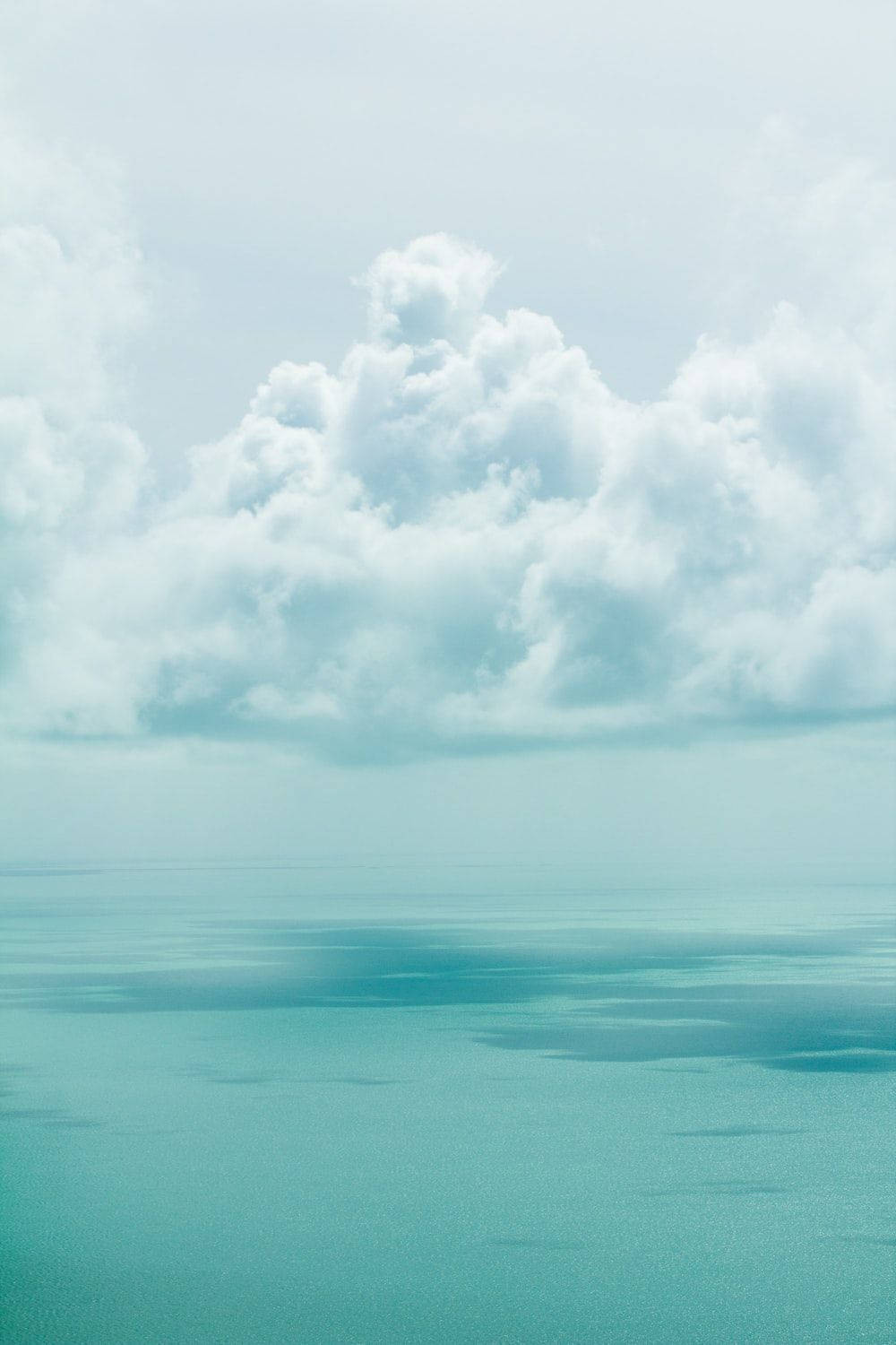 Turks And Caicos 桌布 壁紙 — 廣闊的藍綠色海洋在蒼白的天空下與柔軟的白雲相遇，呈現寧靜的空中景觀。