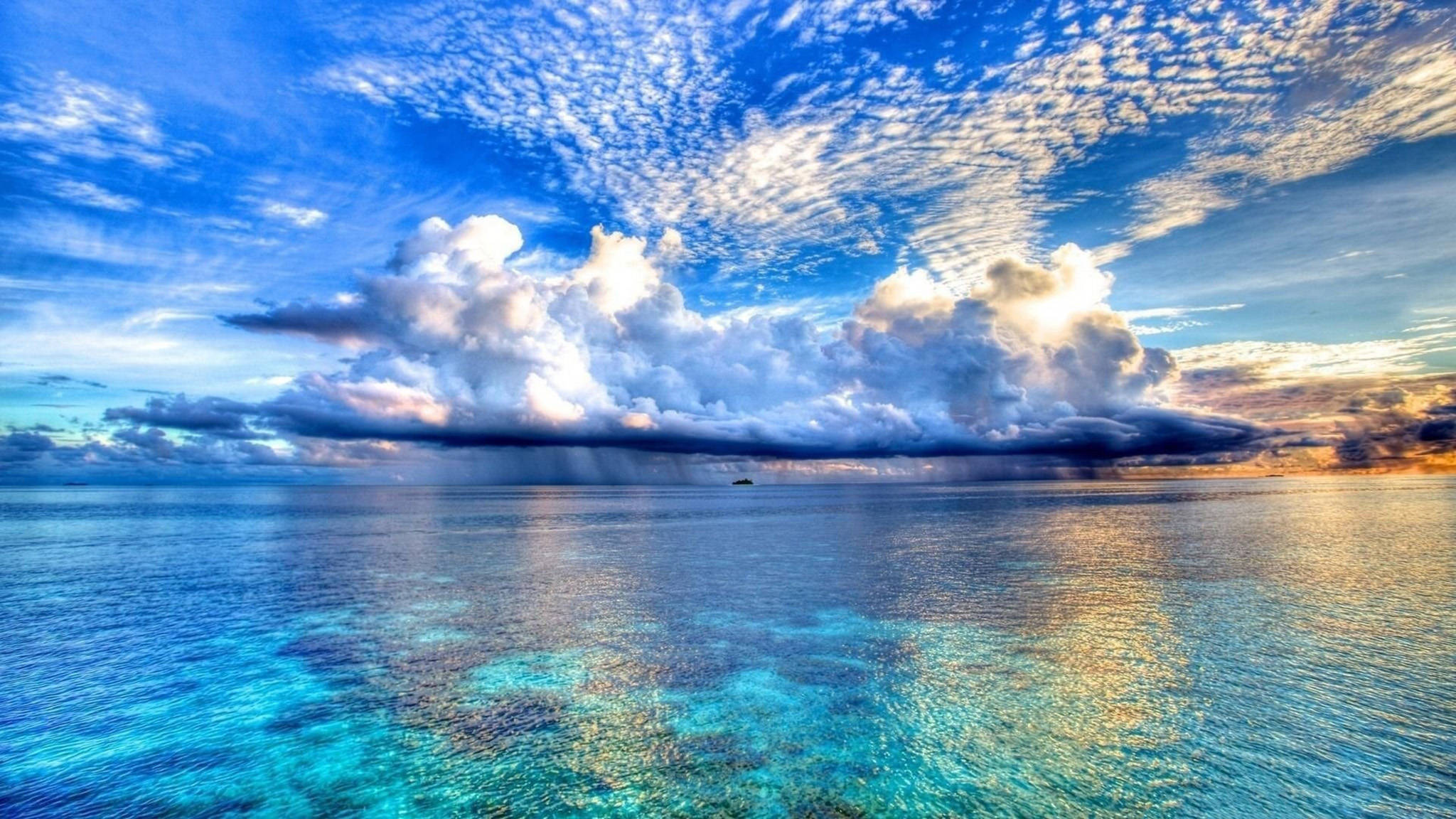View 桌布 壁紙 — 廣闊的藍綠色海洋映照出戲劇性的天空，陽光照射的雲朵和金色的日落色調。