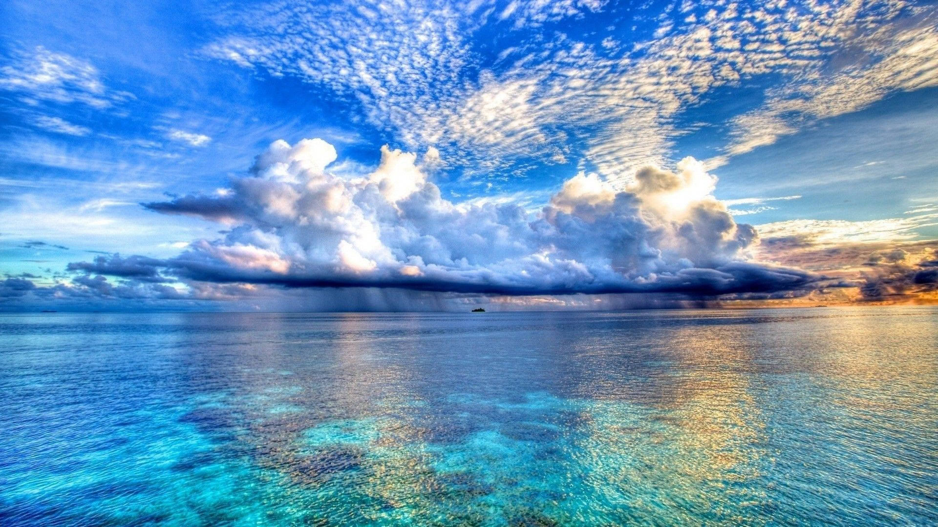 海洋 桌布 壁紙 — 廣闊的藍綠色海洋映照著戲劇性的天空，有蓬鬆的白雲和金色的日落色調。