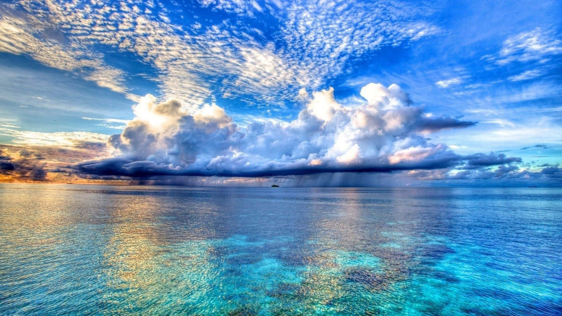 海灘 桌布 壁紙 — 廣闊的藍綠色海洋與戲劇性的天空相遇，陽光照射的雲層和遠處的陣雨籠罩在平靜的水面上。