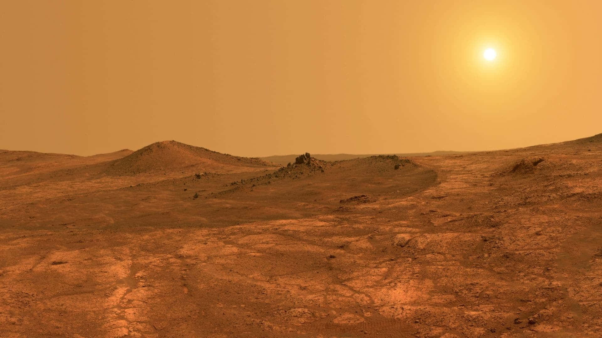 Mars Surface 桌布 壁紙 — 廣闊的鏽紅色火星景觀沐浴在金色陽光下，起伏的沙丘和遠處的岩石露頭在朦朧的橙色天空下。