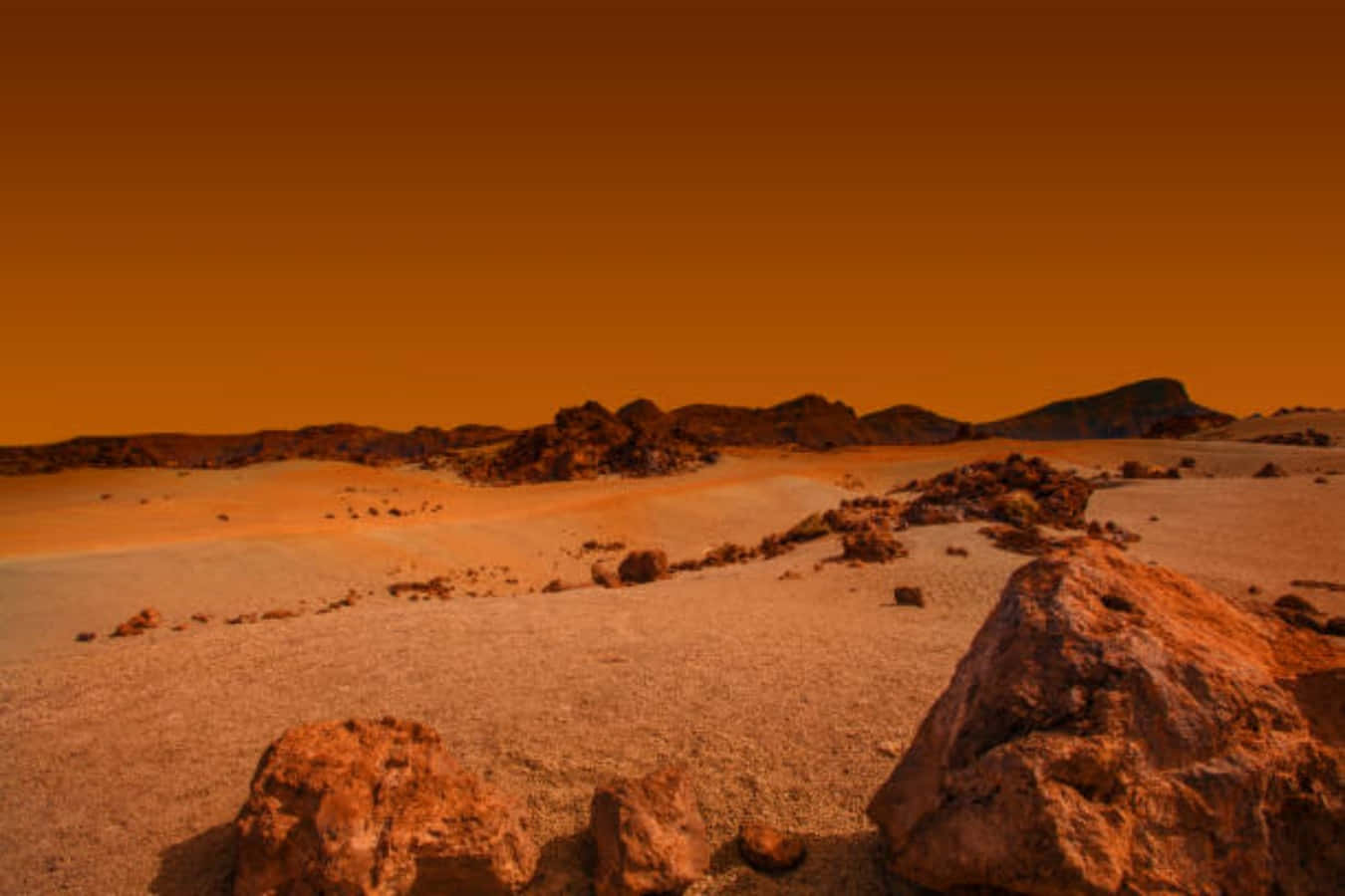 Mars Surface 桌布 壁紙 — 廣闊的鏽色沙漠景觀，朦朧的橙色天空下散佈著巨石和遠處的平頂山。