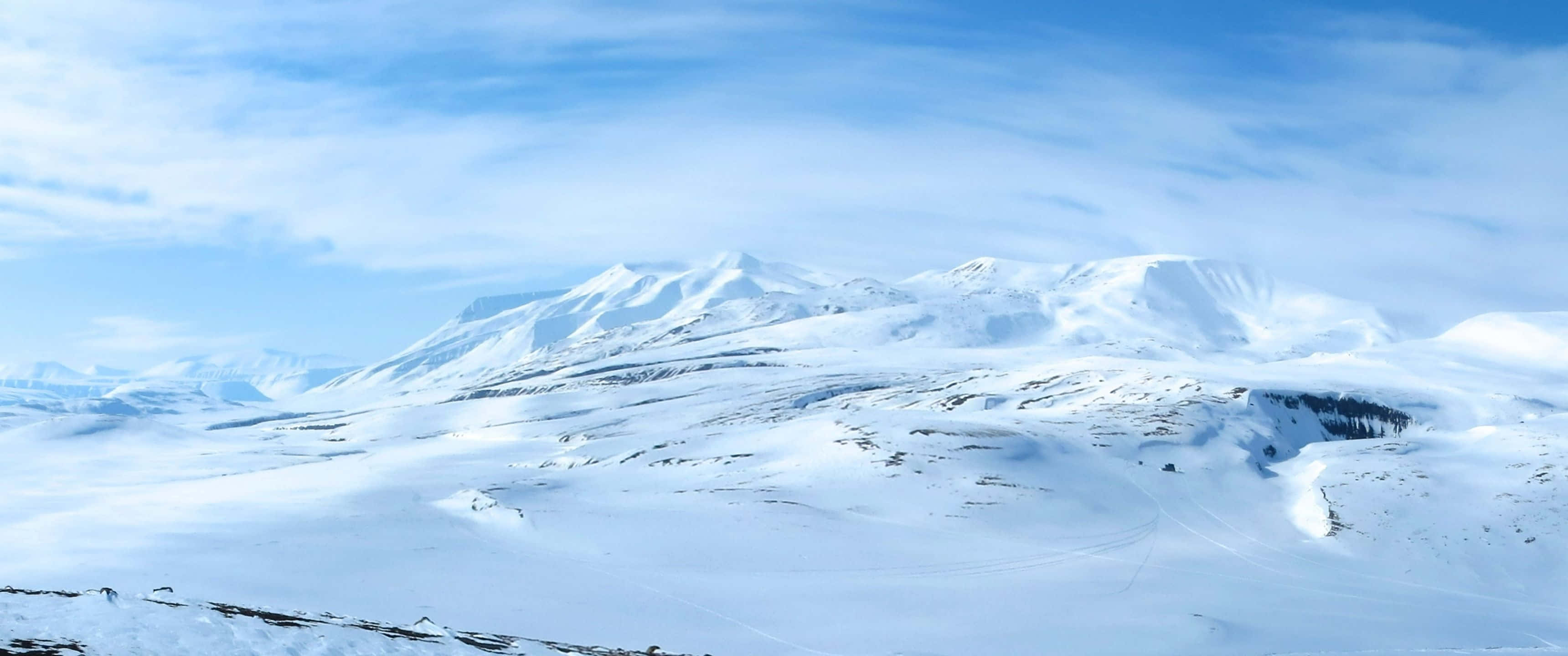 3440x1440 桌布 壁紙 — 廣闊的雪山山脈在明亮的藍天下延伸，天空中有縷縷雲彩。