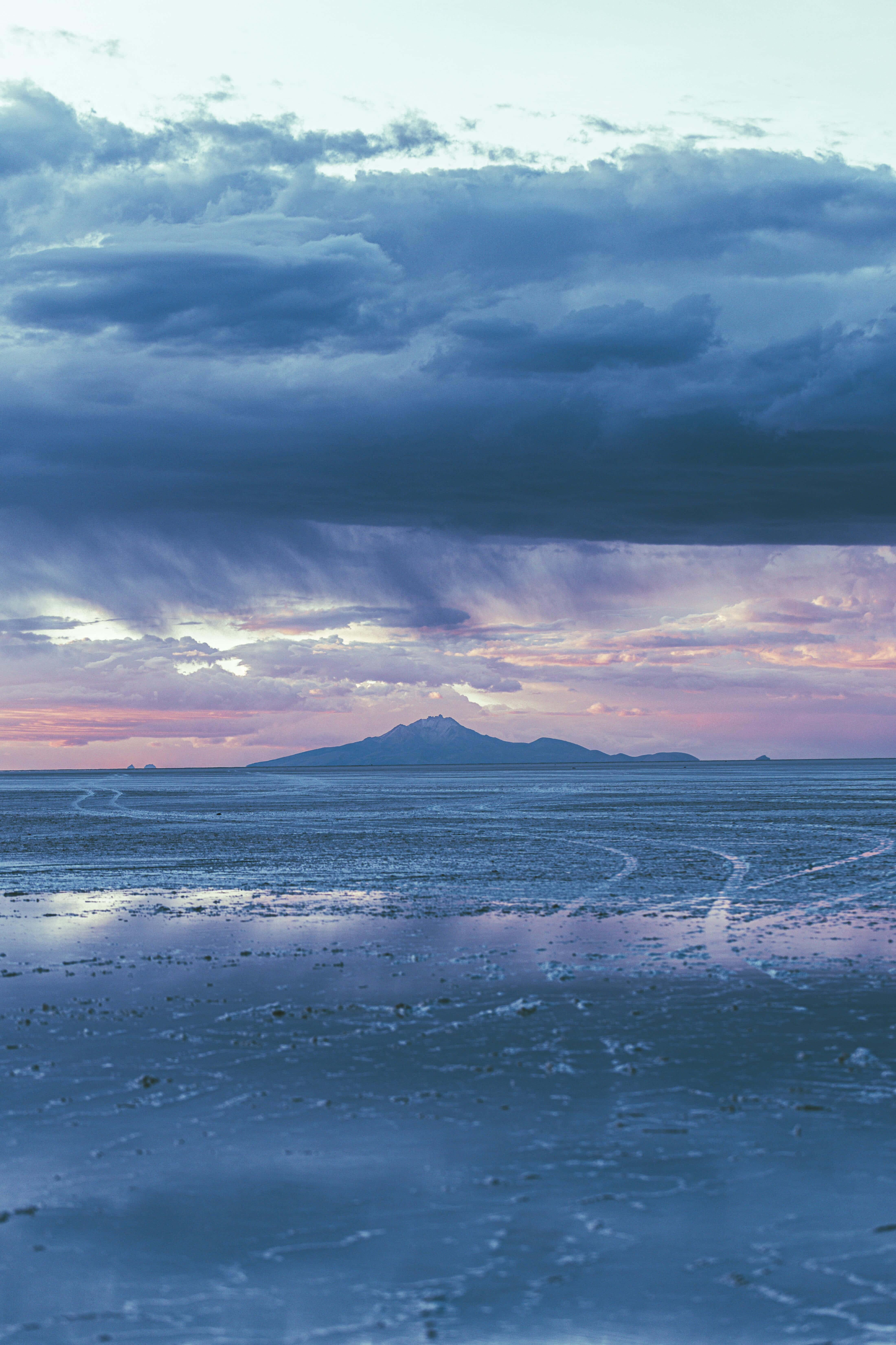 Aesthetic Beachy 桌布 壁紙 — 廣闊的鹽灘反射出戲劇性的暮色天空，帶有紫色雲彩和遠處積雪山峰的輪廓。