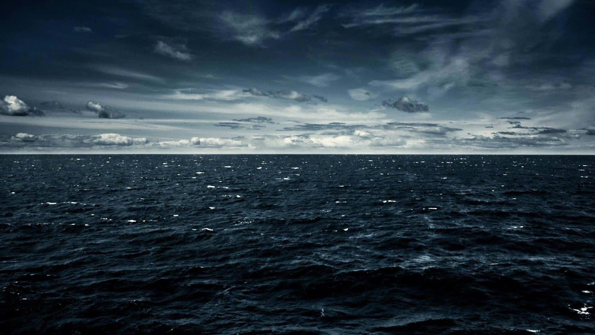 Dark Ocean 桌布 壁紙 — 廣闊的黑暗海洋，在陰沉天空下，散落的雲朵映照在波濤洶湧的水面上。