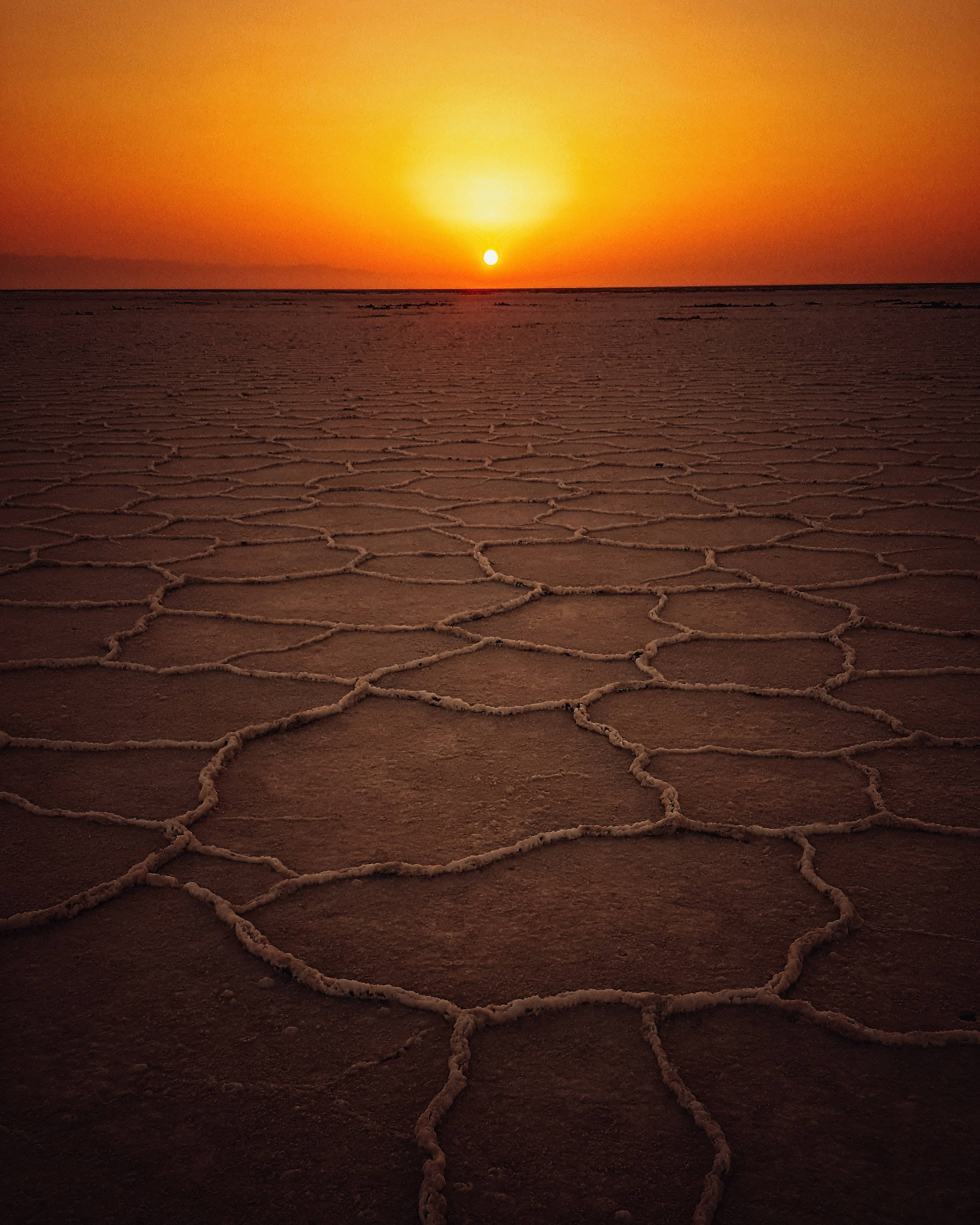 風景 桌布 壁紙 — 廣闊的龜裂鹽灘在熾熱的橙色夕陽下延伸，太陽低掛在地平線上。