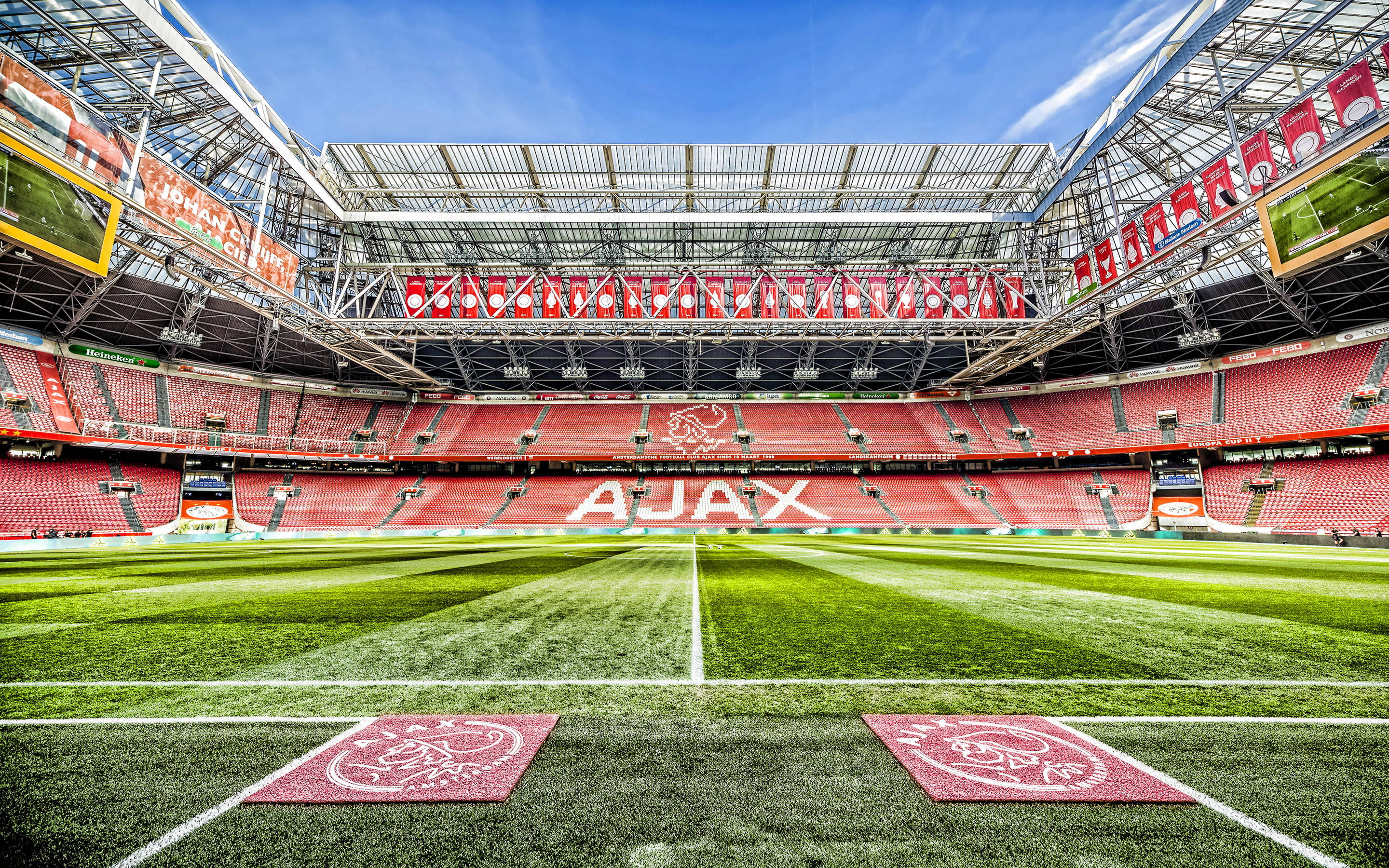 Stadium 桌布 壁紙 — 廣闊空曠的阿賈克斯球場，翠綠草地和紅色座位，在清澈藍天下。