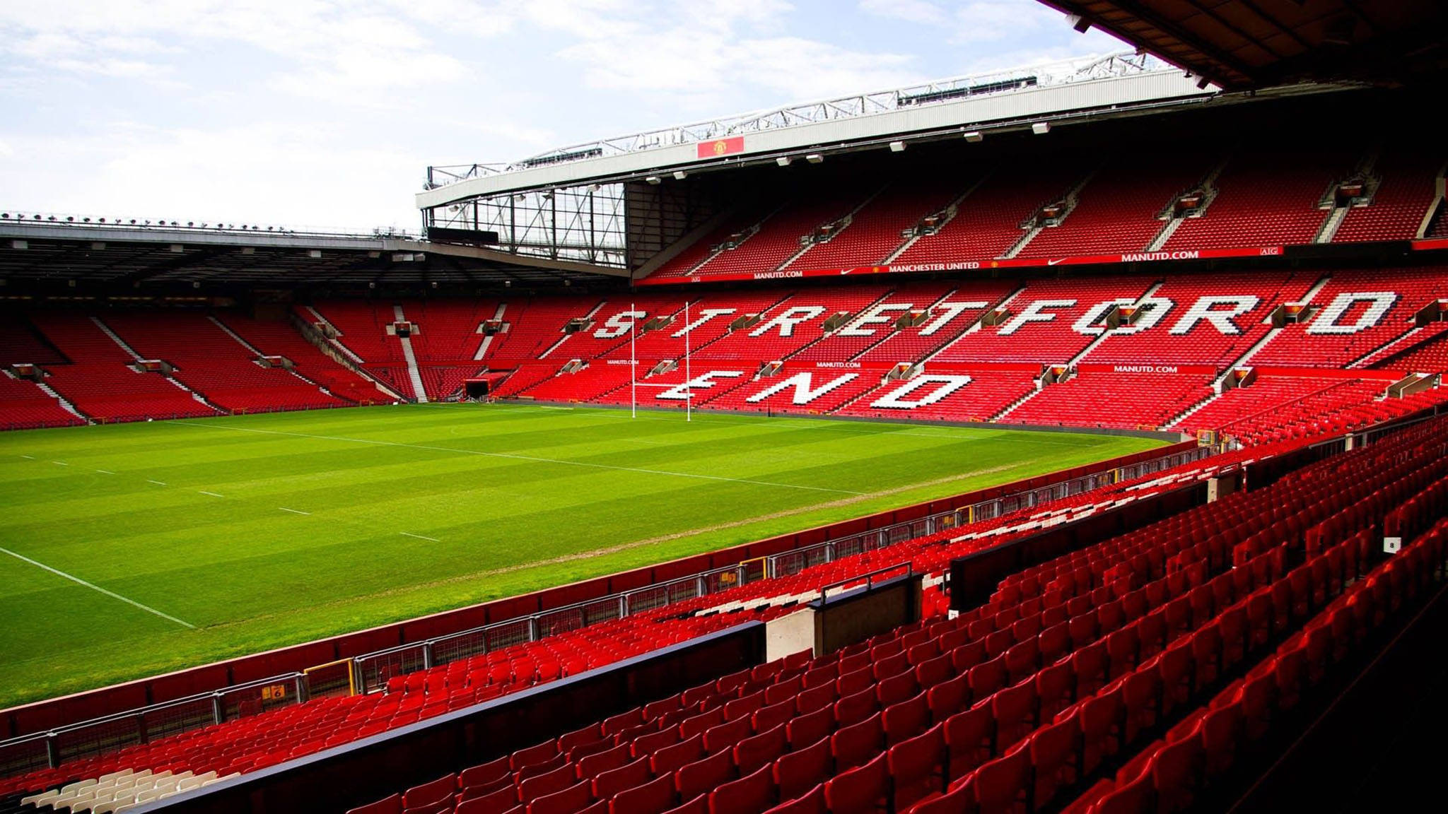 Stadium 桌布 壁紙 — 廣闊空蕩的體育館，設有標誌性紅色座位和 'STRETFORD END' 標牌，俯瞰陰天下 pristine 的綠色足球場。
