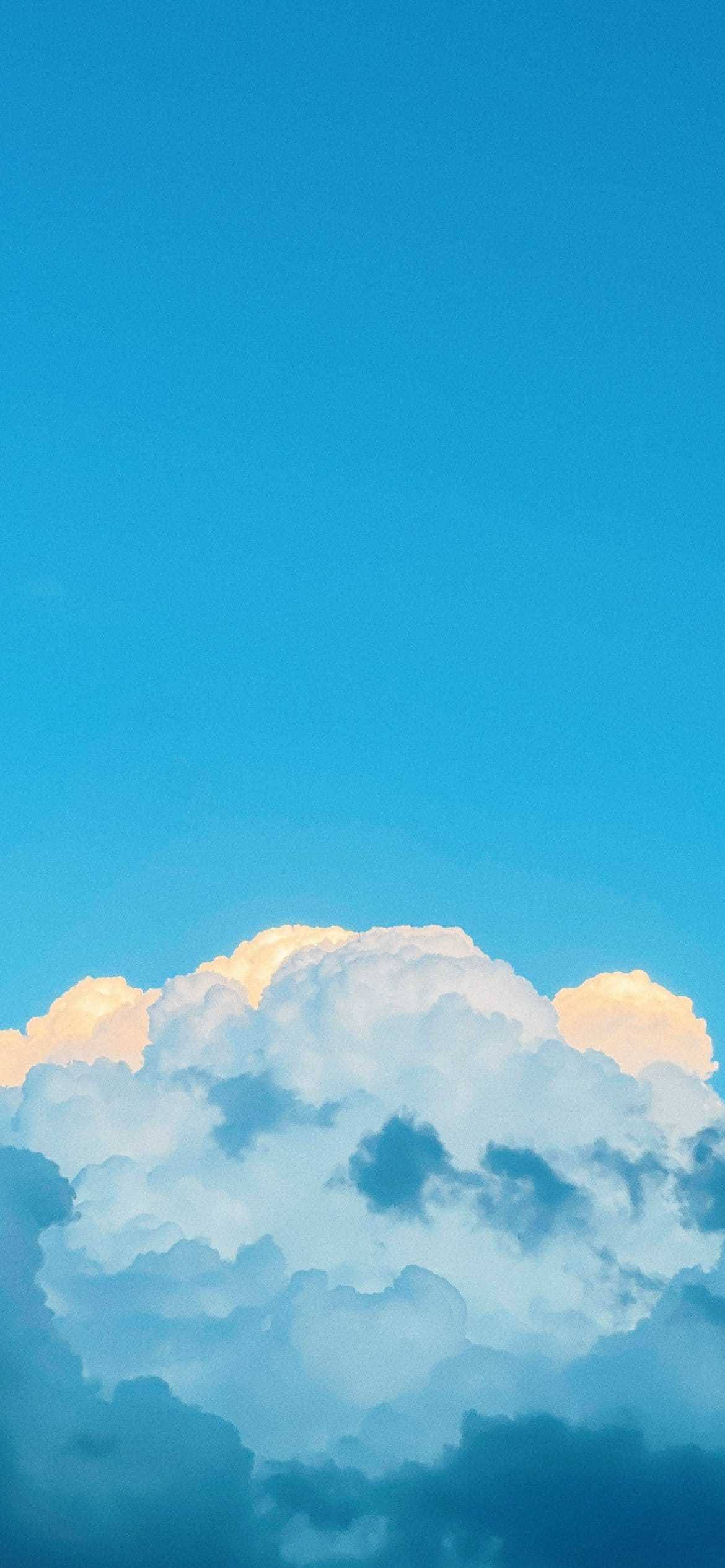 Pastel Blue Aesthetic Tumblr 桌布 壁紙 — 廣闊蔚藍的天空，蓬鬆的白雲在日落地平線上閃耀著金色光芒。