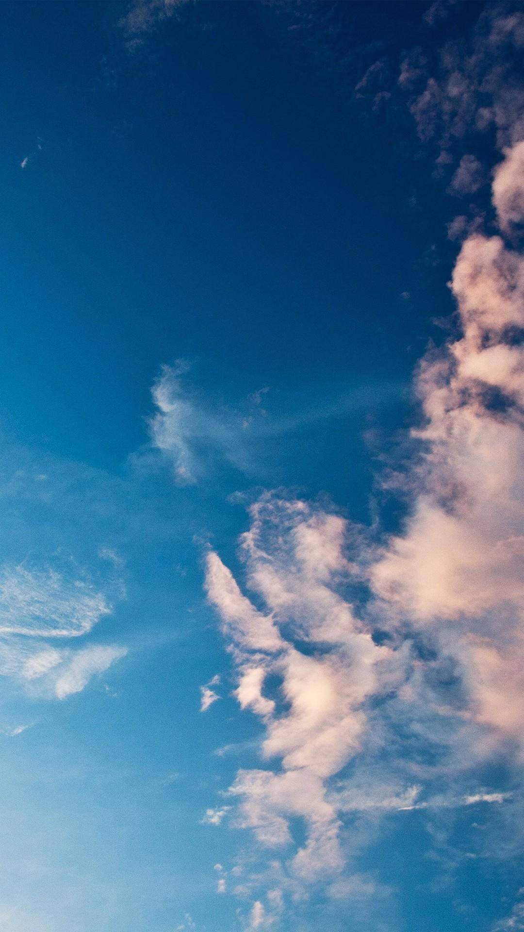 iPhone 桌布 壁紙 — 廣闊蔚藍的天空，點綴著縷縷白雲，近地平線處帶有柔和粉紅色調。