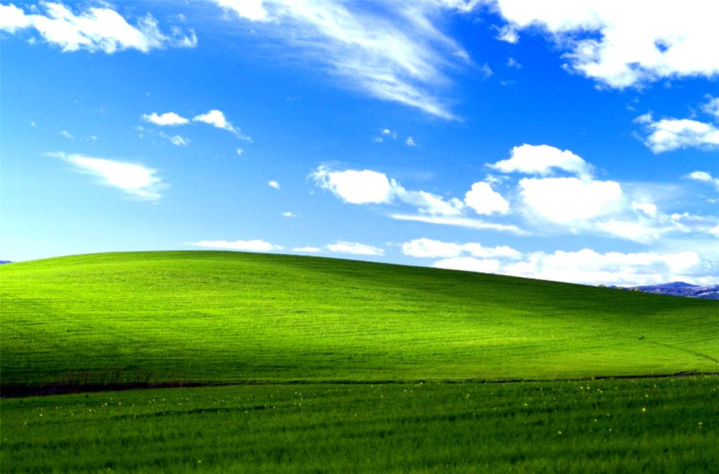 Windows 95 動態圖 桌布 壁紙 — 廣闊起伏的綠色山丘，在明亮的藍天下有蓬鬆的白雲。
