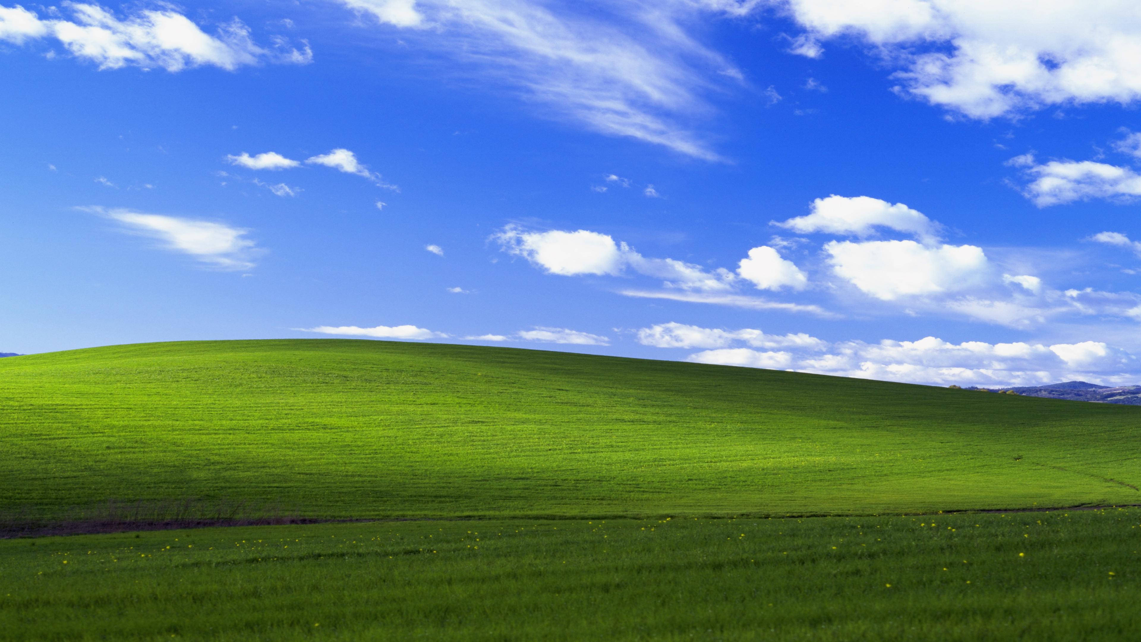 Windows 10 高畫質 桌布 壁紙 — 廣闊起伏的綠色山丘在明亮的藍天下延伸，點綴著蓬鬆的白雲。