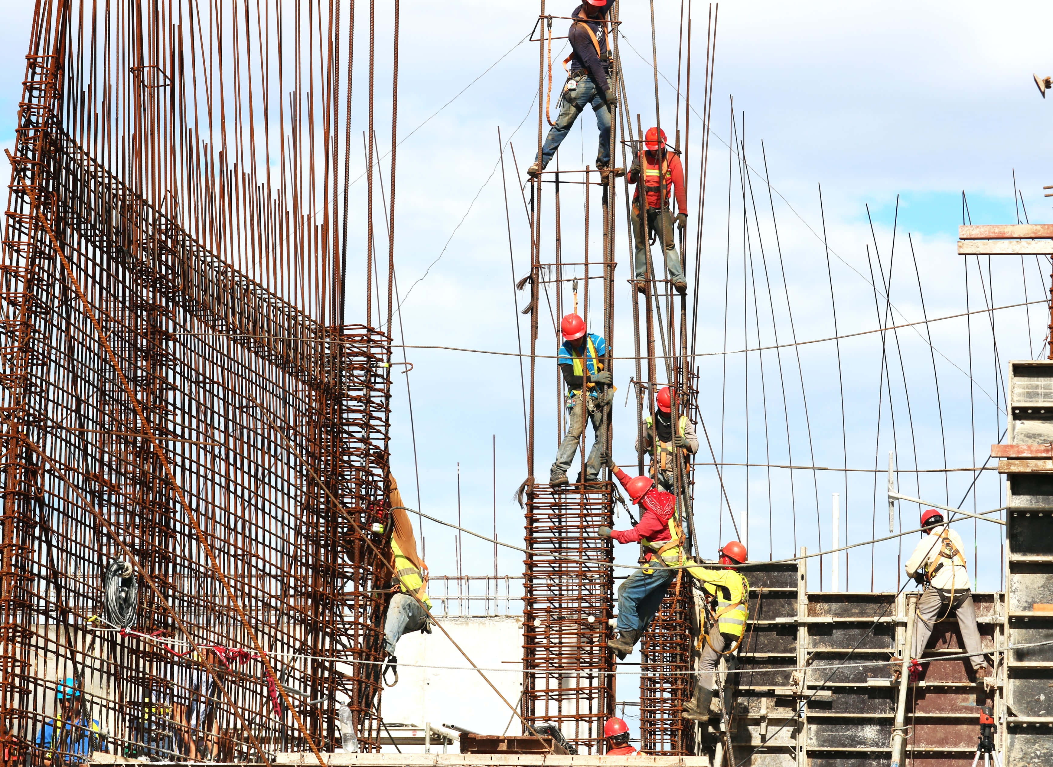 Working 桌布 壁紙 — 建築工人戴著安全帽和安全帶，在明亮的藍天下攀爬高高的鋼腳手架。