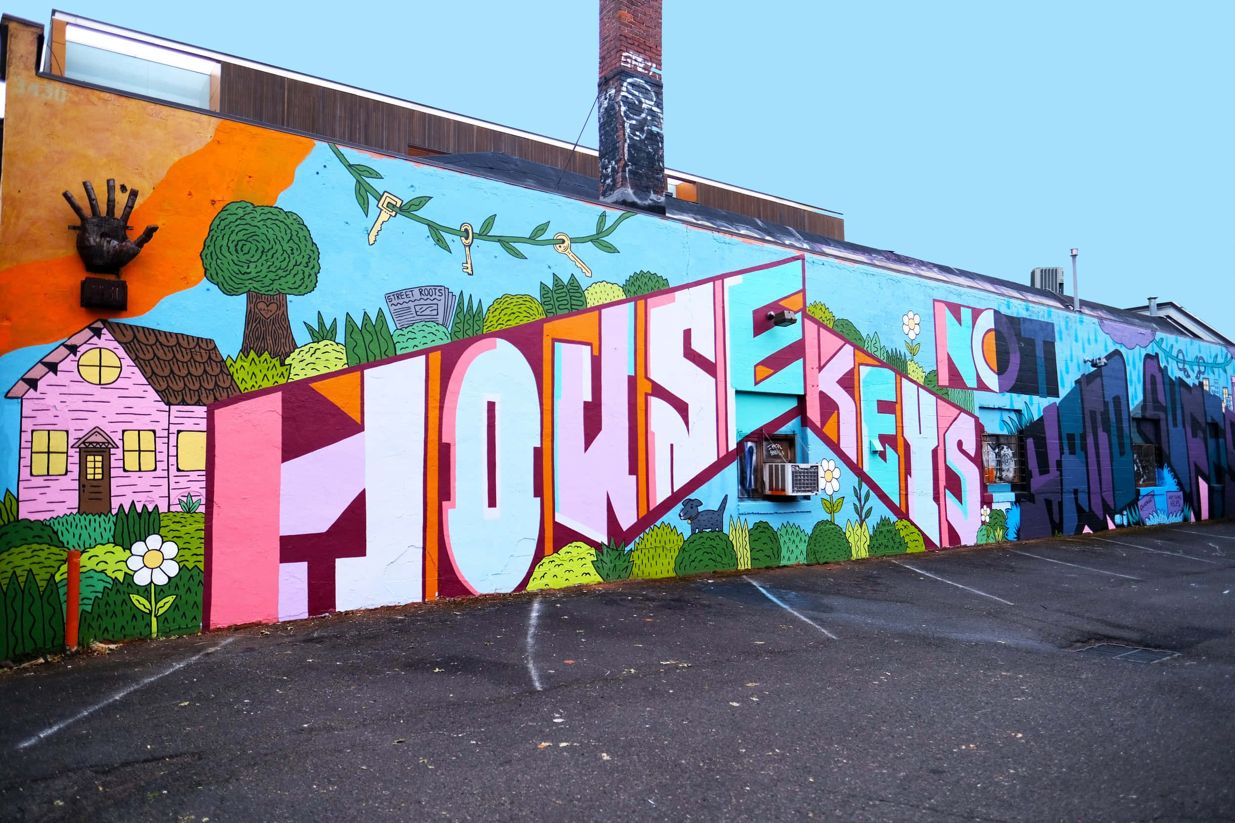 Graffiti Art 桌布 壁紙 — 建築物牆上充滿活力的塗鴉壁畫，以鮮豔的粉紅色和紫色 'HOUSE KEYS' 文字、卡通房屋、樹木和手部藝術為特色，背景是清澈的藍天。