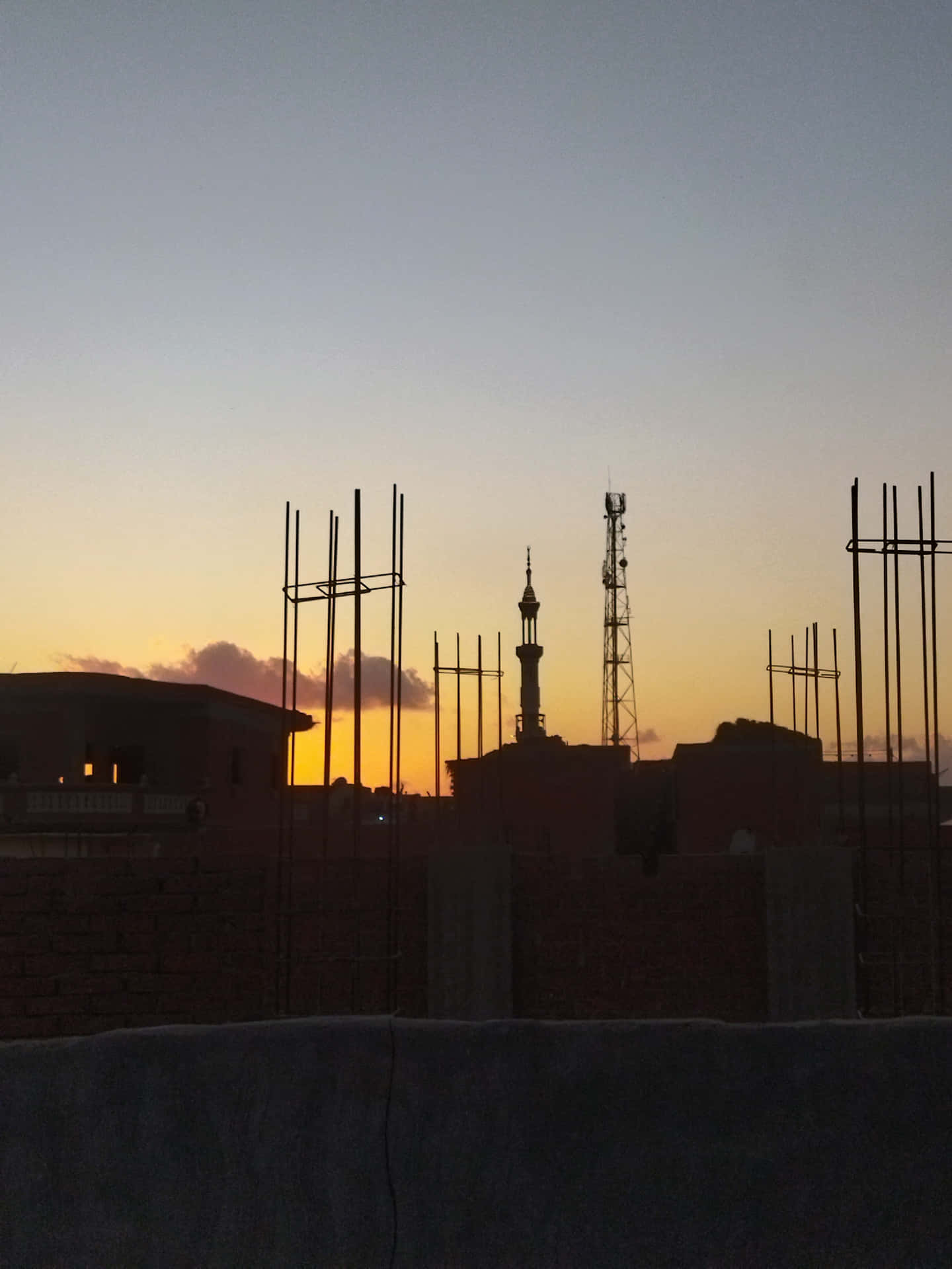wallpaper 壁紙 — 建築鋼筋的剪影框住了清真寺宣禮塔和通訊塔在漸變天空下的日落景色。
