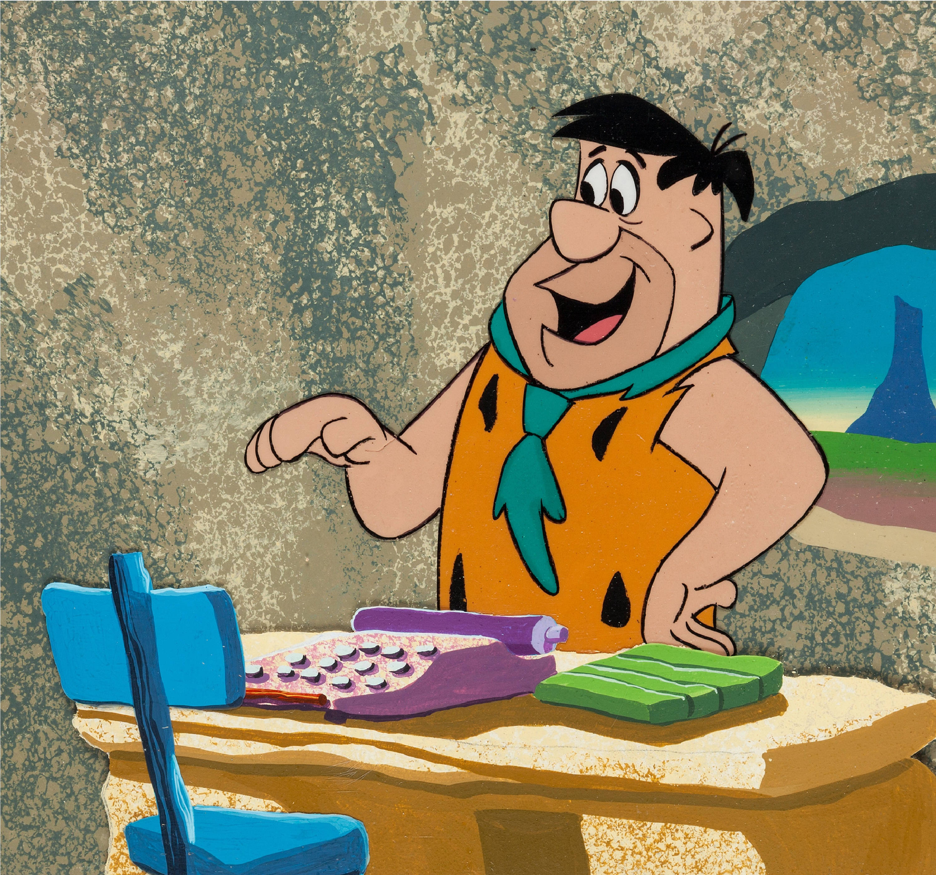 Flintstone 桌布 壁紙 — 弗林斯通在石器時代的書桌前微笑，桌上有一個紫色打字機和綠色積木。