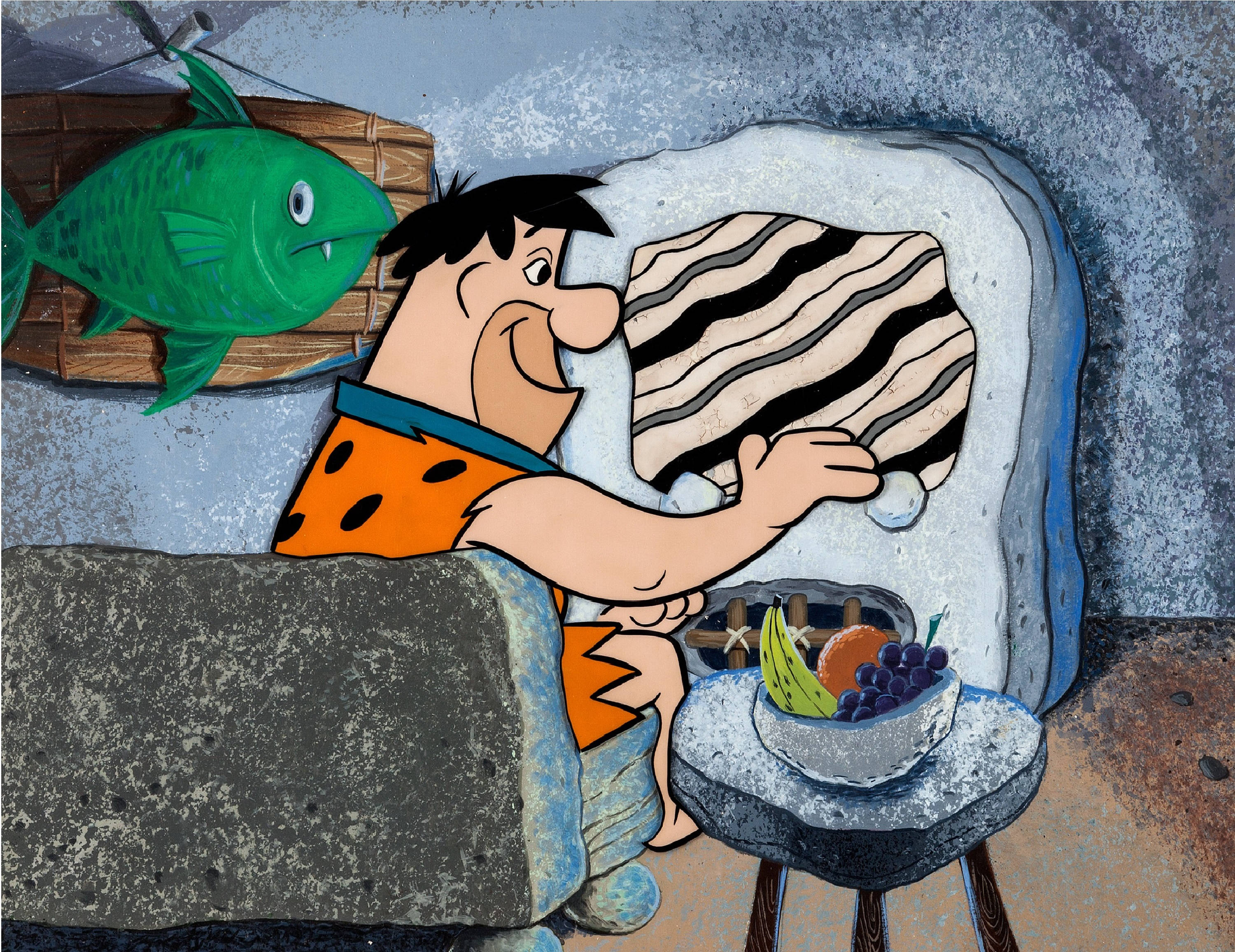 Flintstone 桌布 壁紙 — 弗雷德·燧石在石器時代洞穴中高興地拿著一條斑馬紋毯子，附近有一條綠色的魚和一個水果碗。