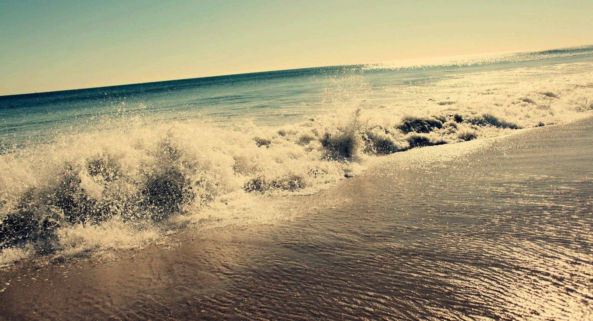 Relaxing Desktop 桌布 壁紙 — 強勁的海浪在晴朗的天空下拍打著陽光明媚的沙灘，濺起閃閃發光的水花。