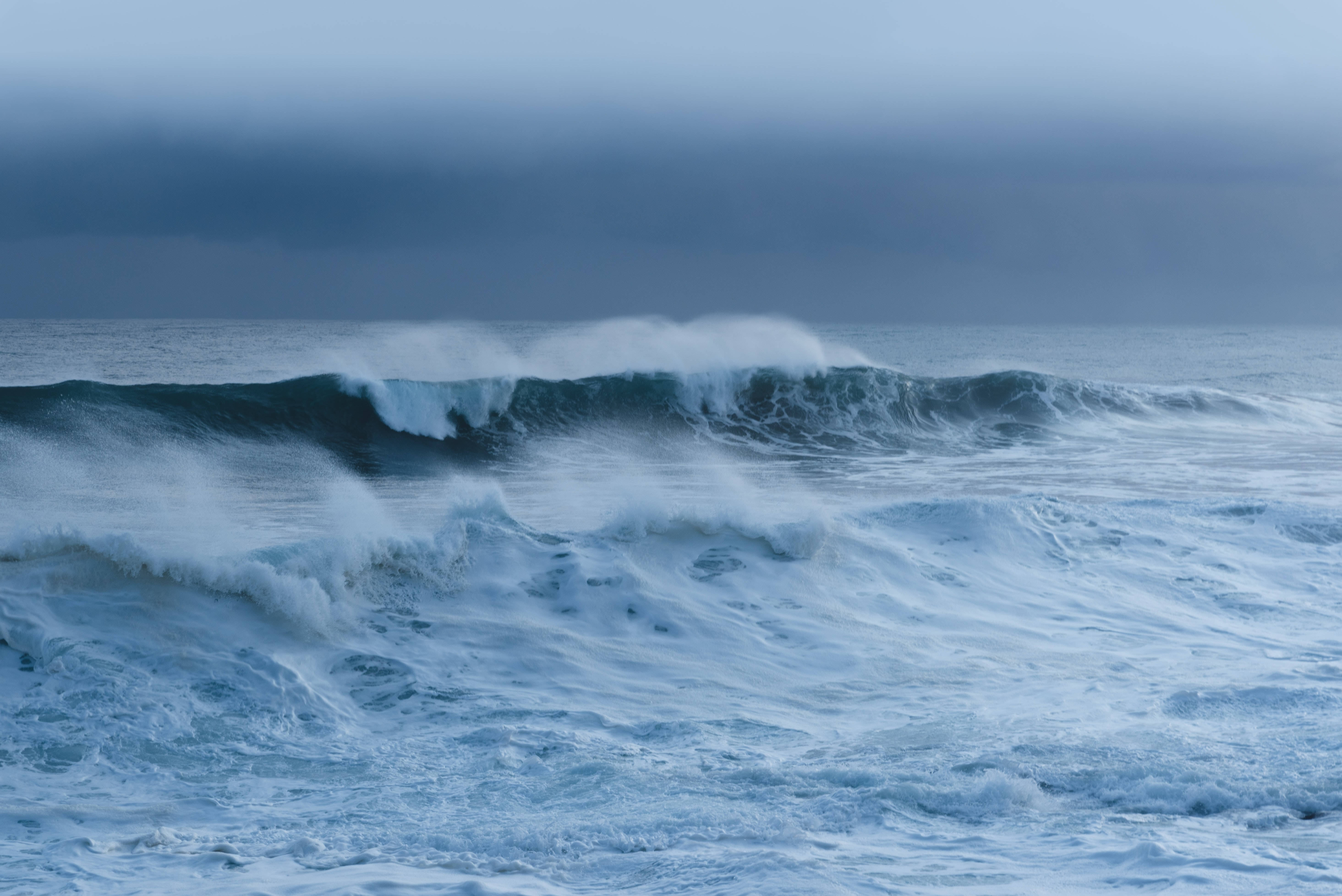 暴風 桌布 壁紙 — 強勁的海浪在沉重的暴風雨天空下破碎，形成戲劇性的單色藍色場景。