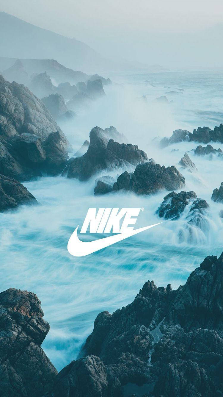 Nike iPhone 桌布 壁紙 — 強勁的海浪拍打著堅固的海岸岩石，天空迷濛，中央有一個醒目的白色Nike標誌。
