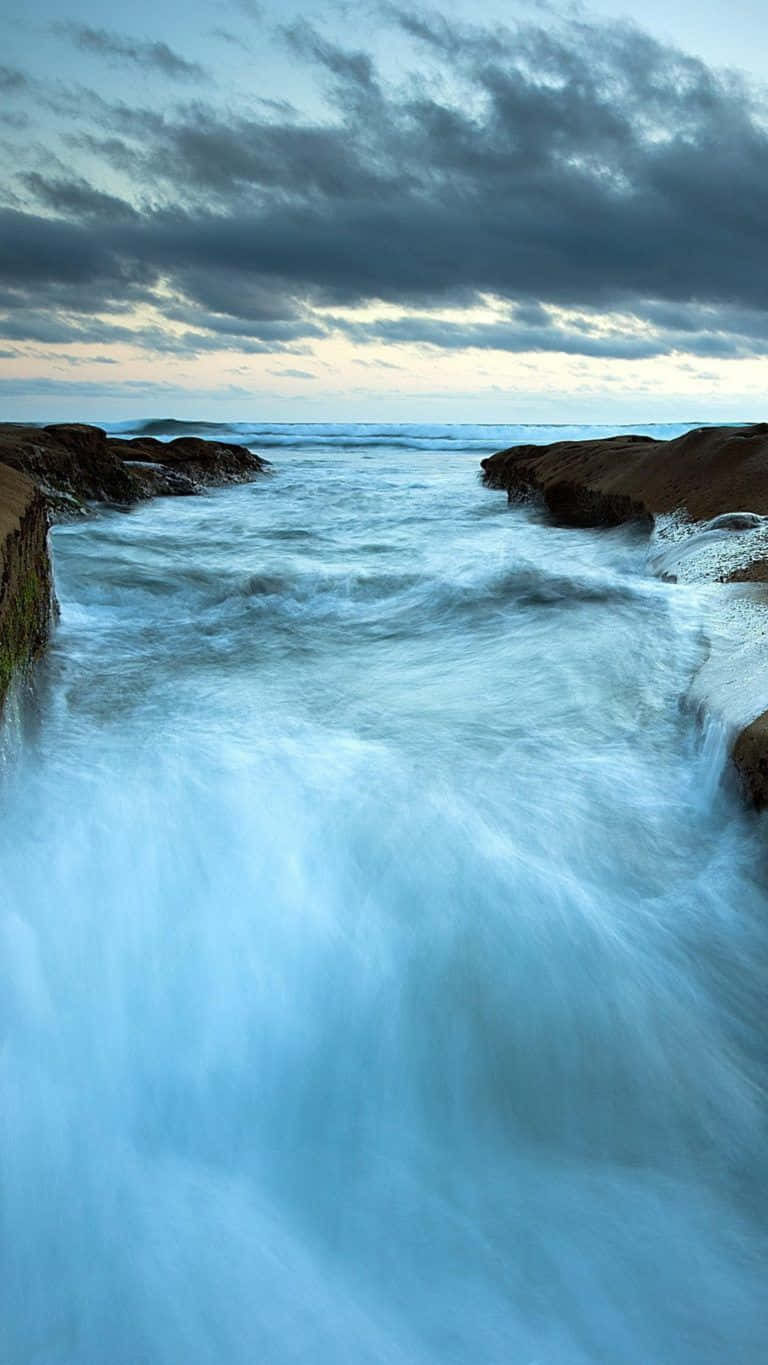 Wave 桌布 壁紙 — 強勁的海浪衝擊崎嶇的懸崖，天空陰沉，暮色中雲層條紋分明。