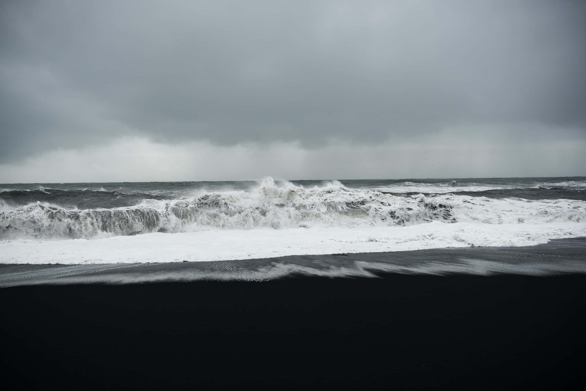 Dark Ocean 桌布 壁紙 — 強勁的白色波浪在沉重的灰色暴風雨天空下衝擊著黑色的火山海灘。