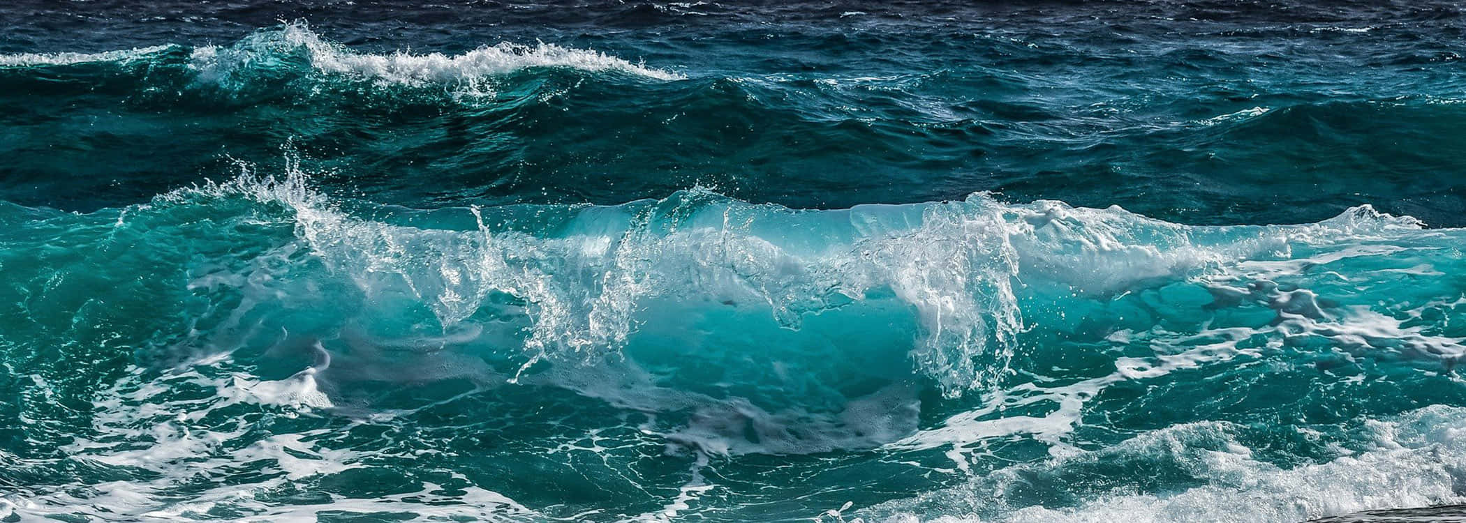 Blue Ocean 桌布 壁紙 — 強勁的綠松色海浪在明亮的陽光下撞擊深藍色的大海，激起白色泡沫。
