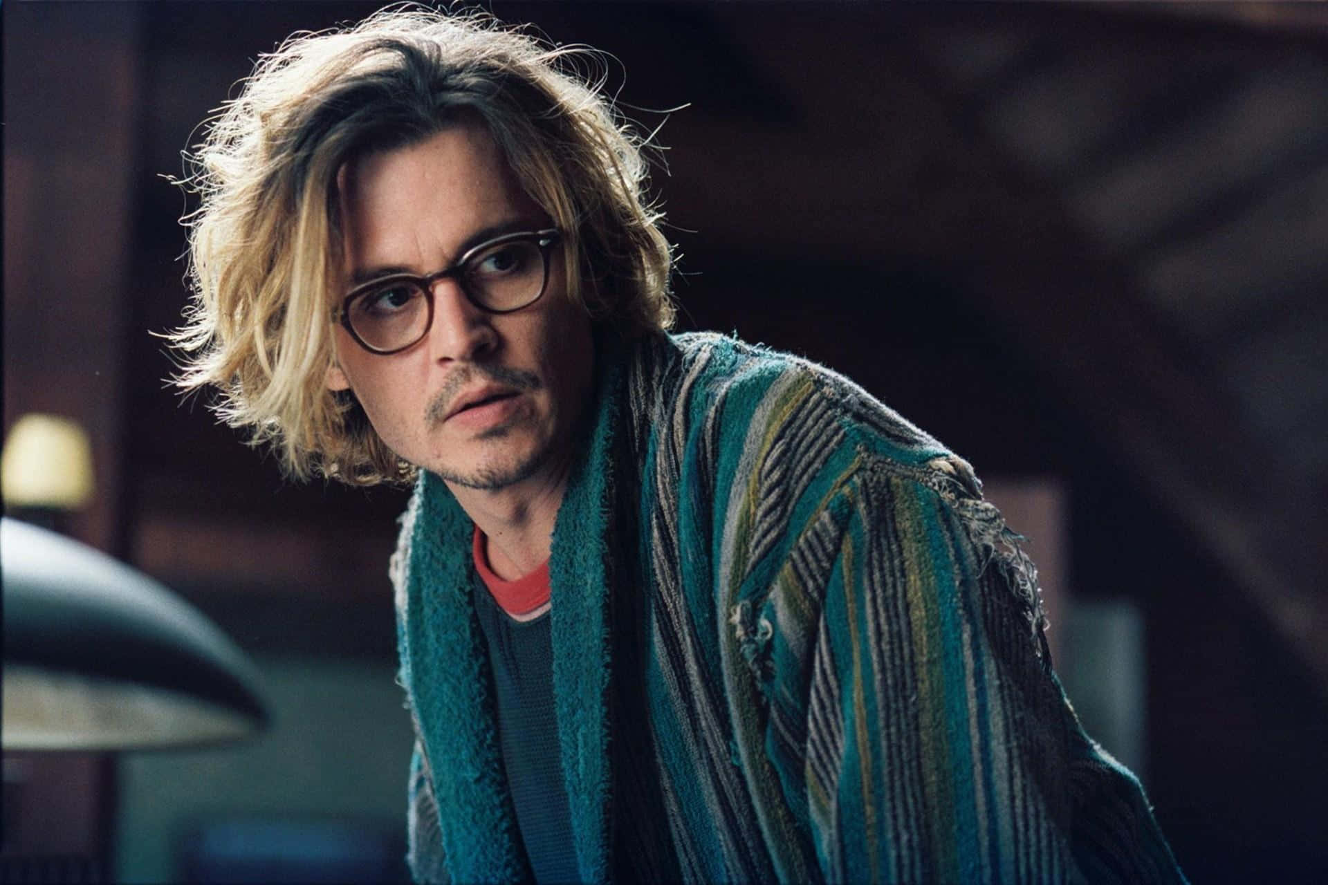 強尼·戴普 桌布 壁紙 — 強尼戴普一頭凌亂金髮，戴著眼鏡，在昏暗的房間裡穿著一件條紋青綠色長袍。
