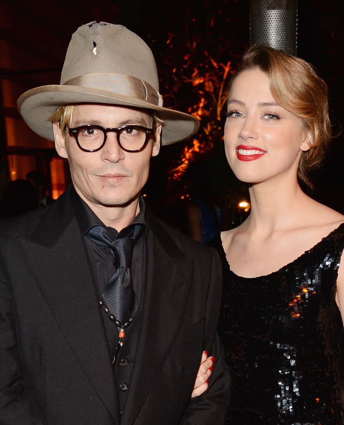 Johnny Depp And Amber Heard 桌布 壁紙 — 強尼戴普和安柏赫德在溫暖的環境燈光下，穿著時尚的正裝，在一個迷人的晚間活動中一起擺姿勢。