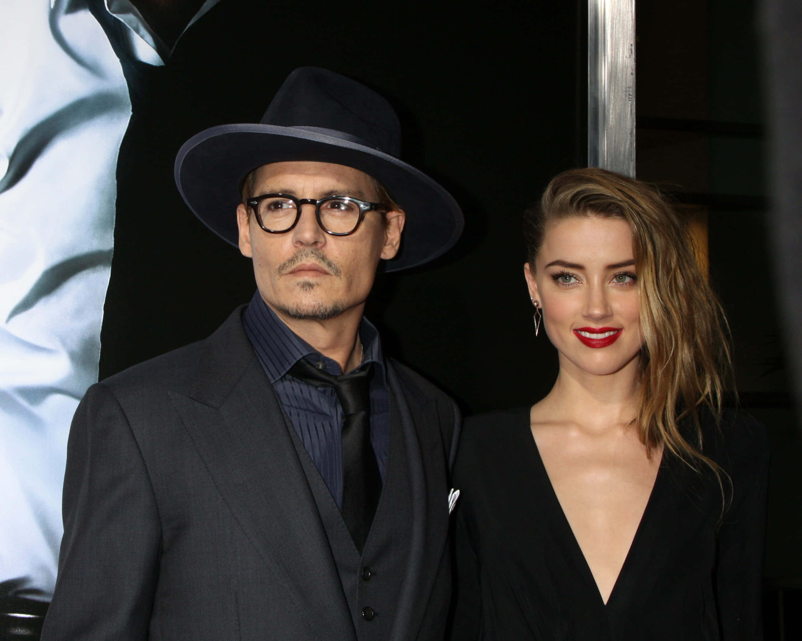 Johnny Depp And Amber Heard 桌布 壁紙 — 強尼戴普和安柏赫德在黑色背景下穿著深色西裝和鮮豔紅唇，在活動中正式擺姿勢。