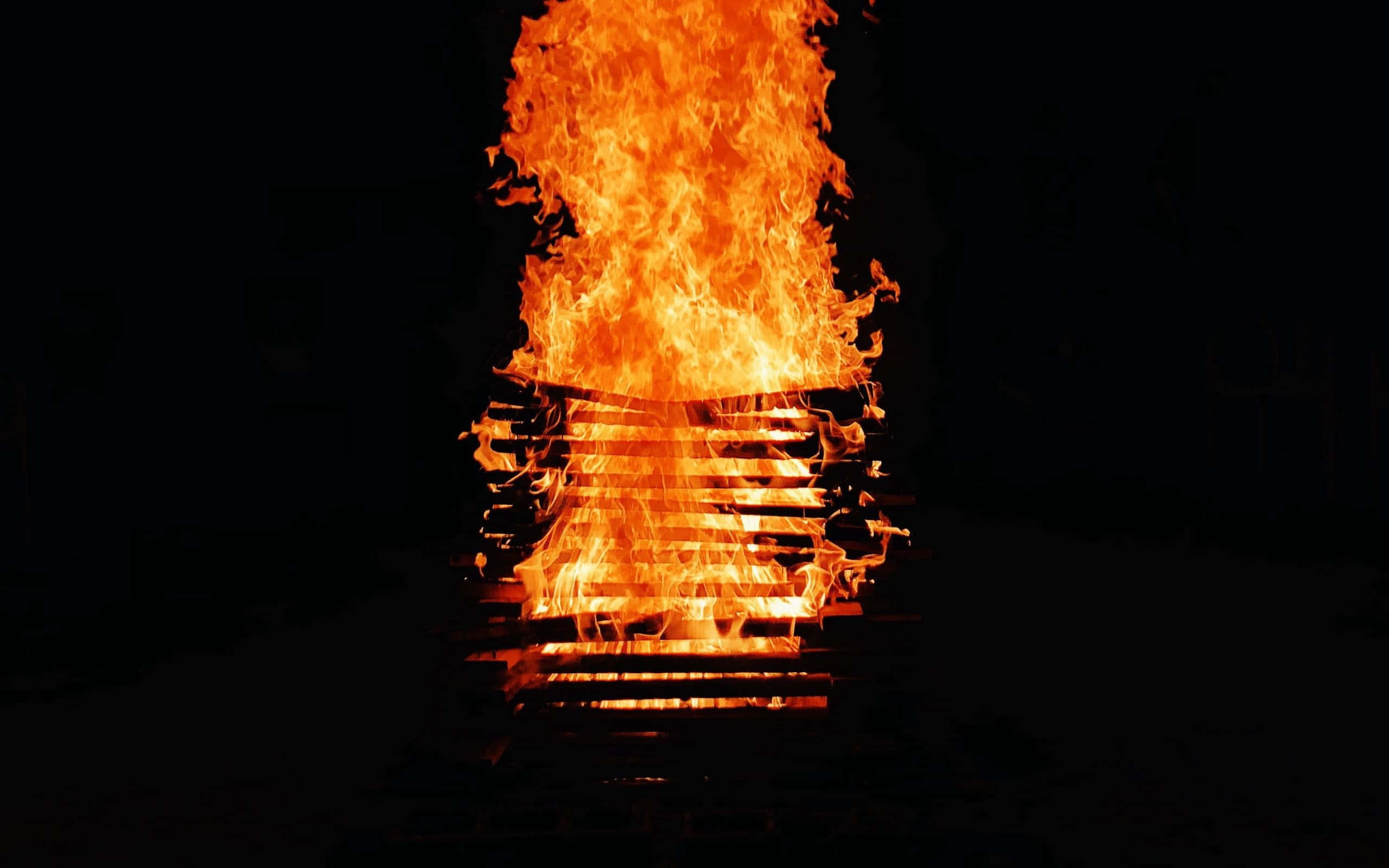 Burn 桌布 壁紙 — 強烈的橙色火焰從一堆燃燒的木棧板上猛烈向上翻騰，背景是漆黑的。