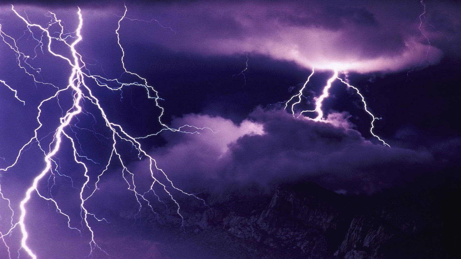 Aesthetic Lightning 桌布 壁紙 — 強烈的紫色閃電在黑暗雲層下，於鋸齒狀山峰上方暴風雨的天空中分叉。