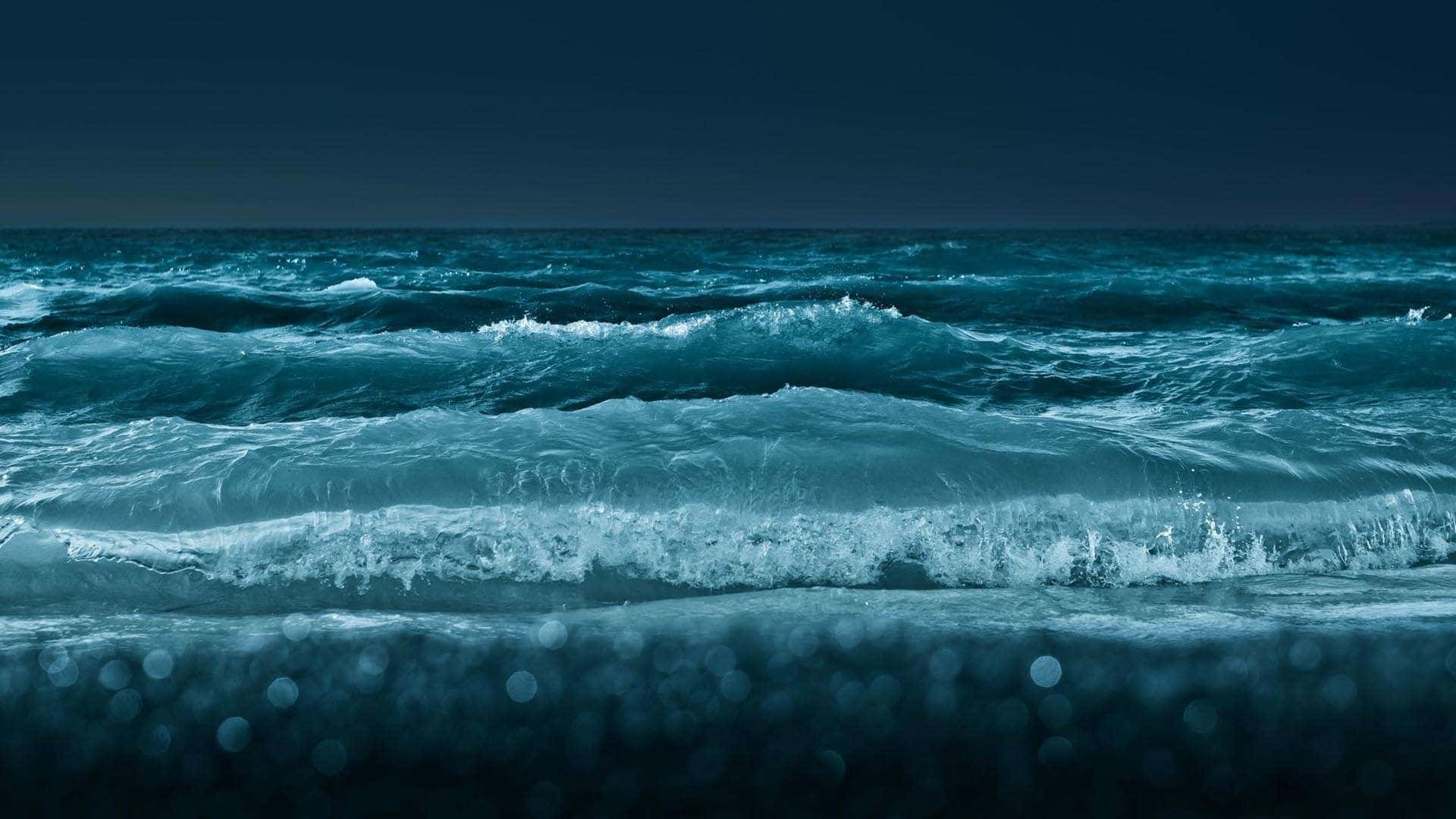 top 桌布 壁紙 — 強烈的藍綠色海浪在暴風雨的夜空下拍打黑暗的海岸，前景帶有散景效果。