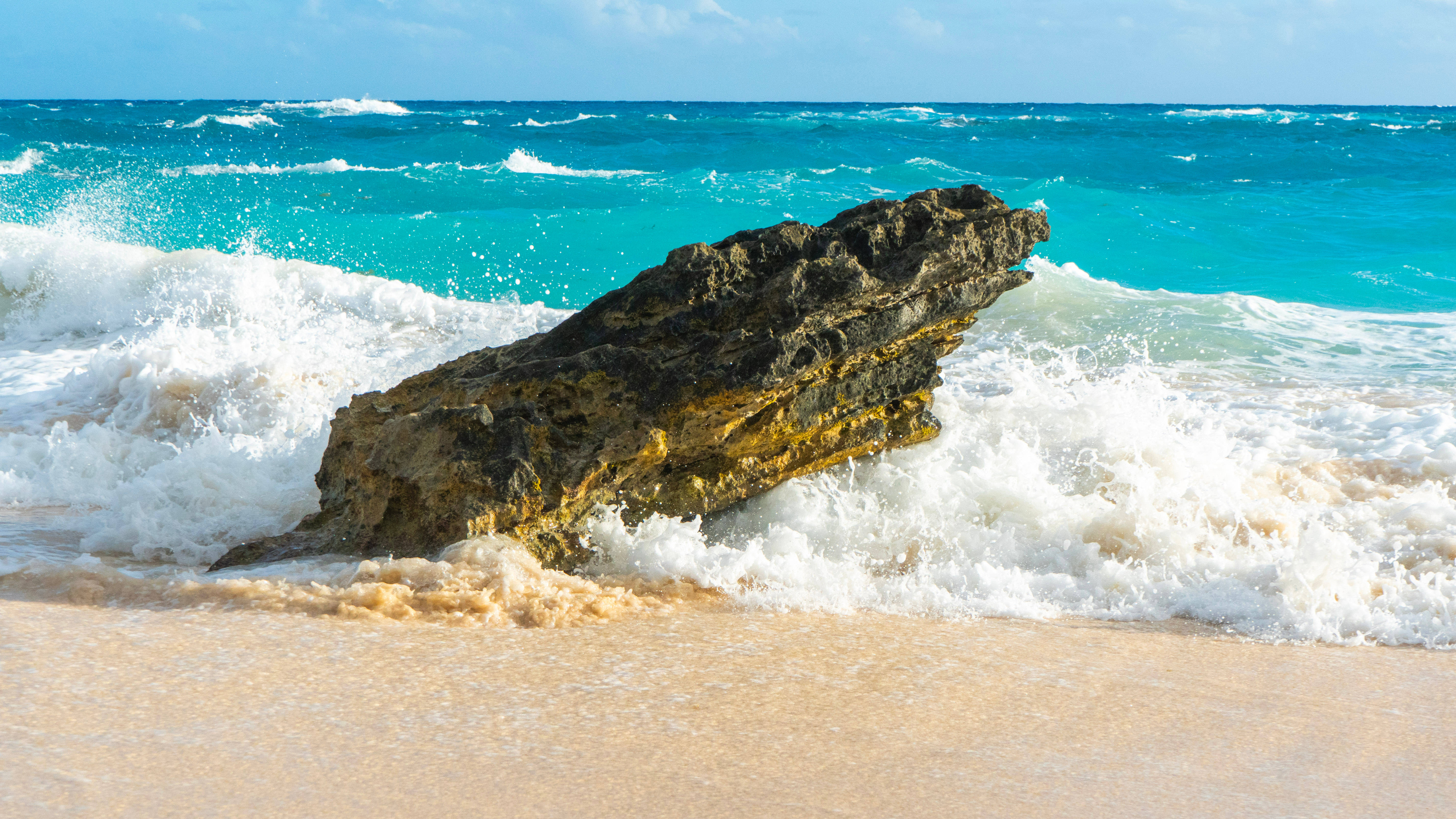 Bermuda 桌布 壁紙 — 強烈的藍綠色海浪拍打著陽光沙灘上堅固的深色岩石。