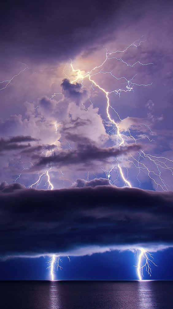 閃電 桌布 壁紙 — 強烈的閃電在黑暗海洋上方的暴風雨紫色天空中劈啪作響，照亮了戲劇性的雲層並反射在水面上。