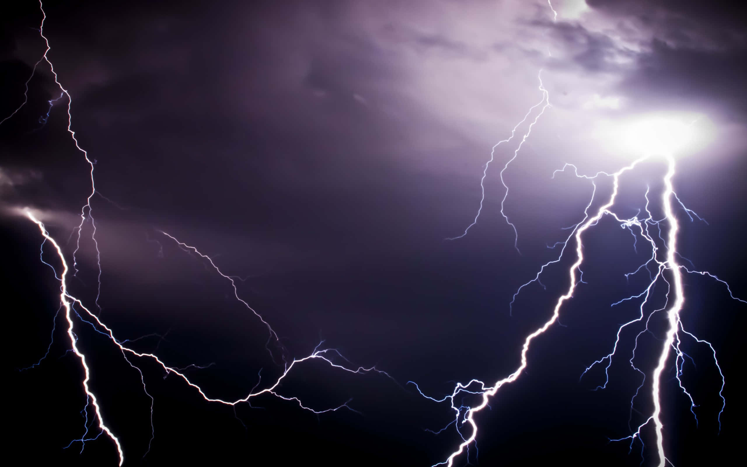 閃電 桌布 壁紙 — 強烈的閃電在黑暗的暴風雨天空中劈啪作響，生動的紫色和白色閃光照亮了雲層。