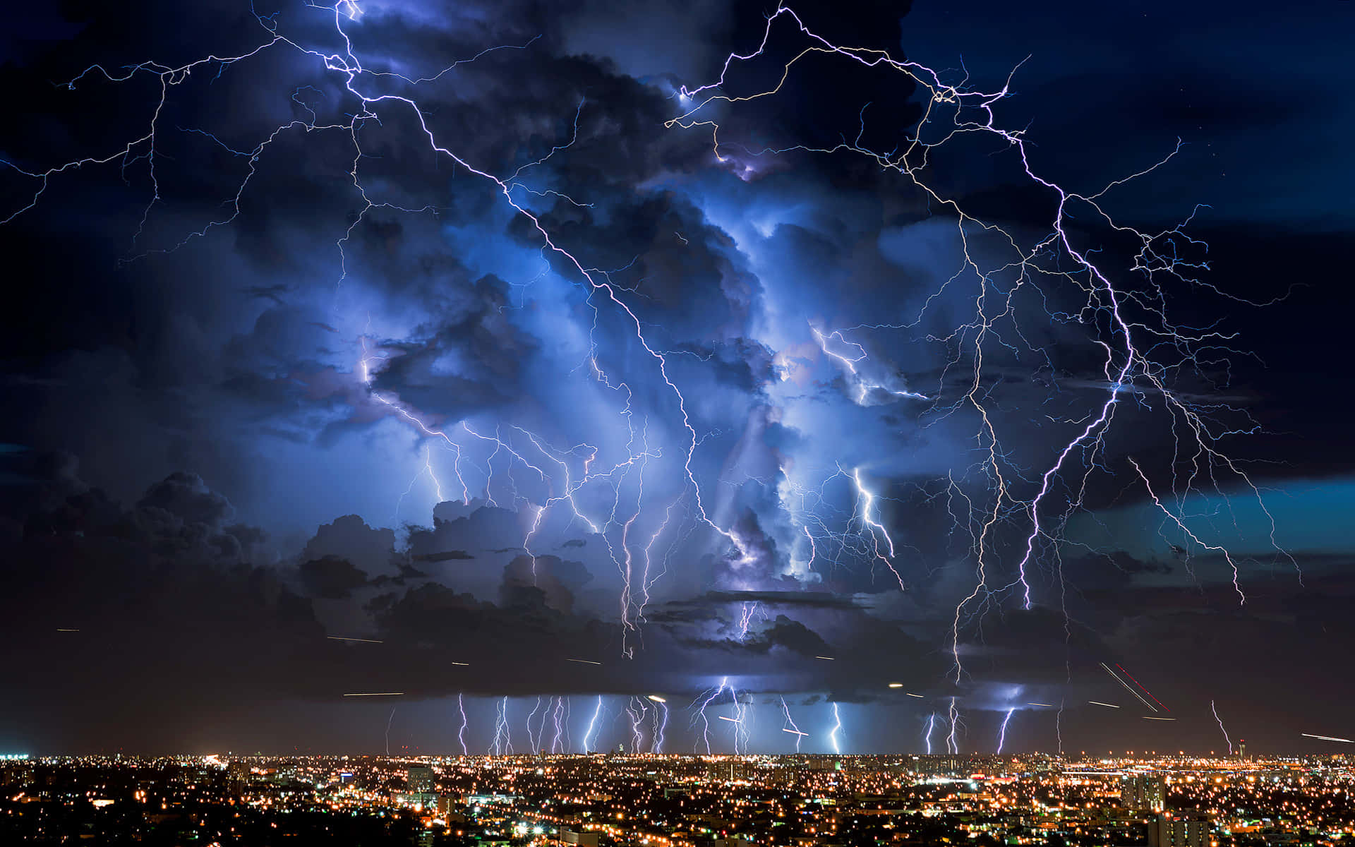 閃電 桌布 壁紙 — 強烈的閃電照亮了暴風雨夜空中廣闊的城市景觀，城市景觀閃爍著人造燈光。