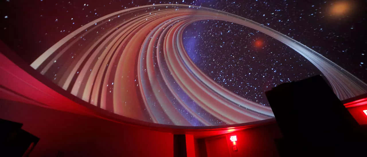 Planetarium 桌布 壁紙 — 彎曲的圓頂天花板展示了一個漩渦星系投影，在黑暗背景下帶有星星和發光帶。