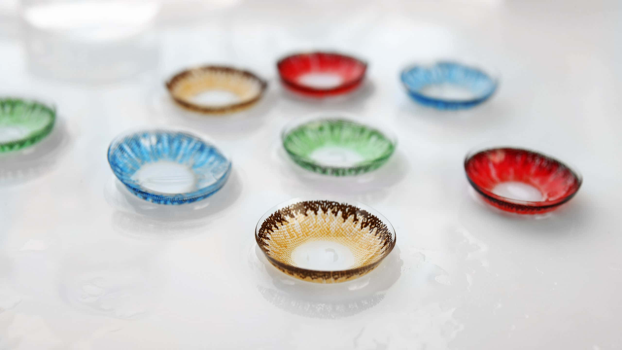 2560x1440 動態圖片 桌布 壁紙 — 彩色玻璃隱形眼鏡盒排列在潮濕的白色表面上，帶有柔和反射。