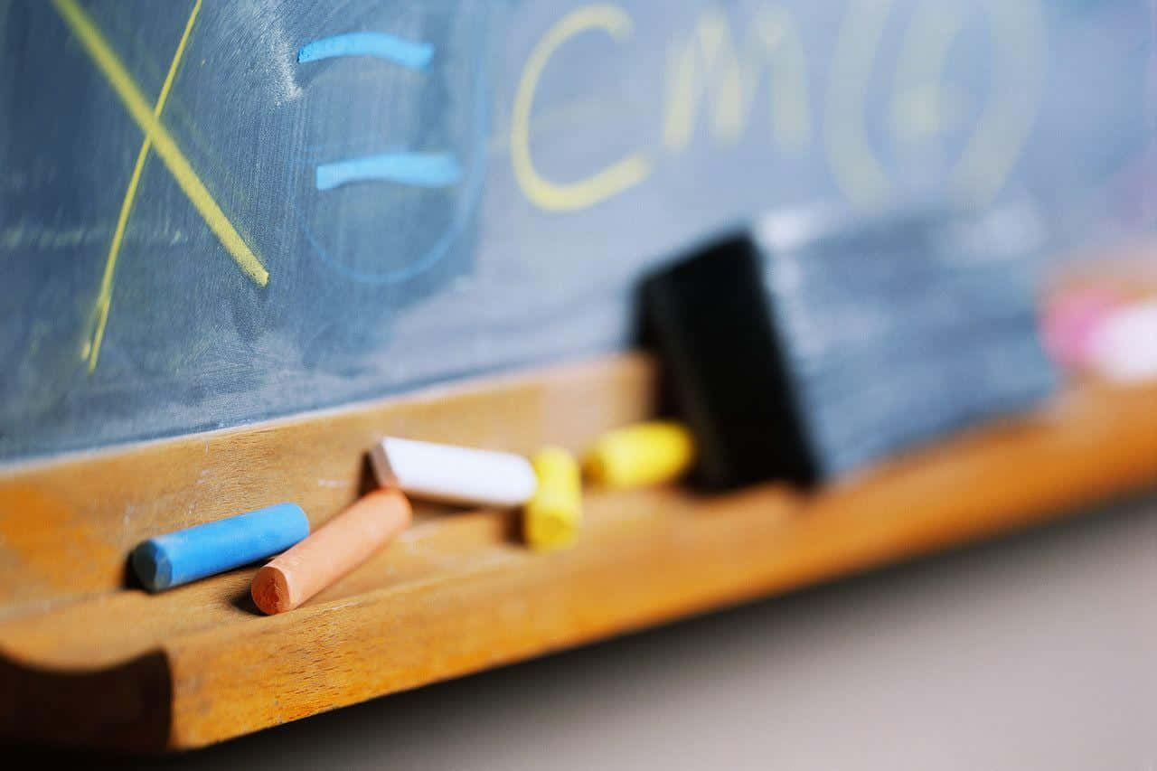 Educational 桌布 壁紙 — 彩色粉筆的特寫，放在木製邊緣上，下方是帶有褪色數學方程式的黑板。