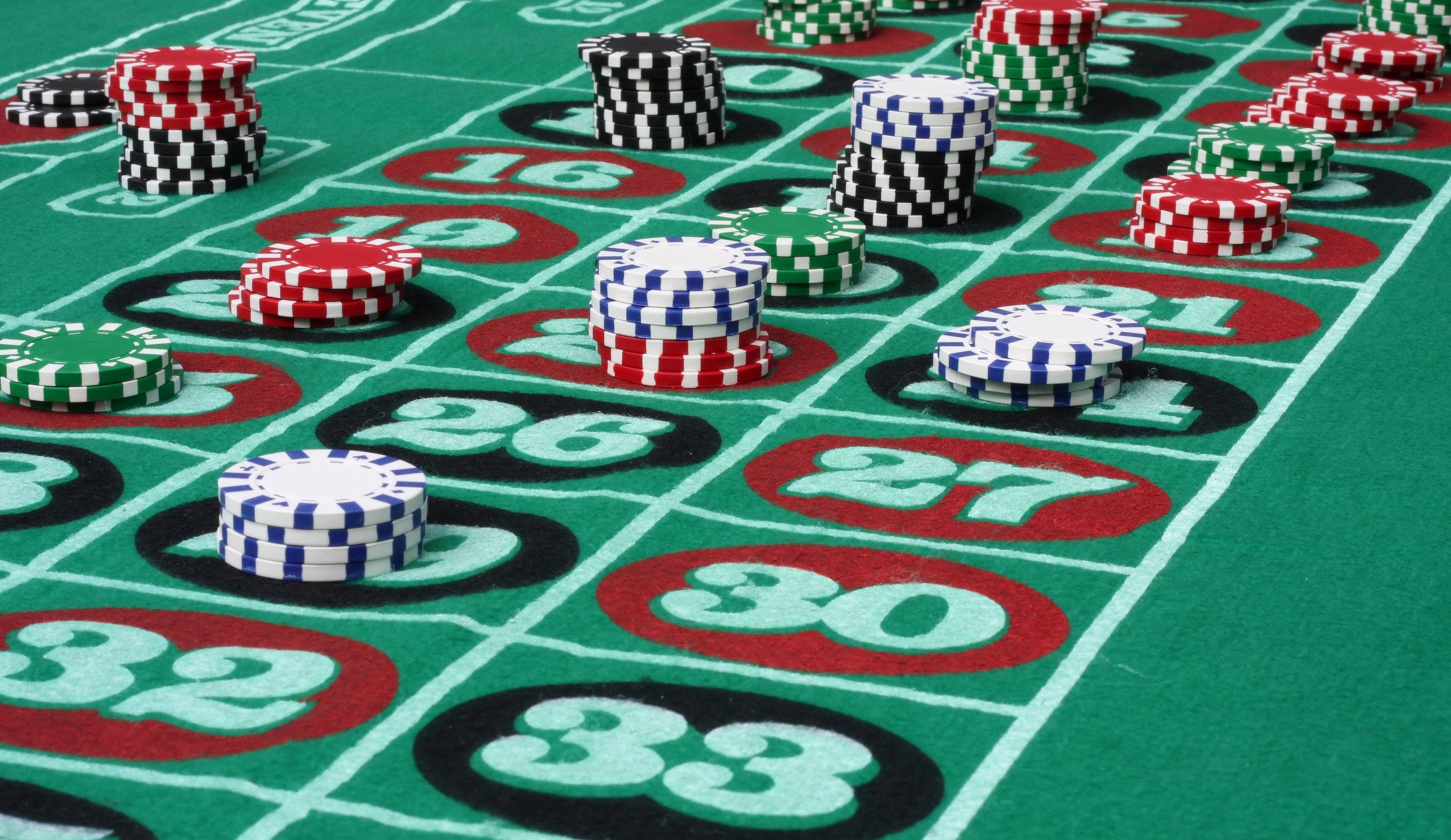 Poker 桌布 壁紙 — 彩色賭場籌碼堆疊在帶有編號投注位的綠色輪盤桌上的特寫。