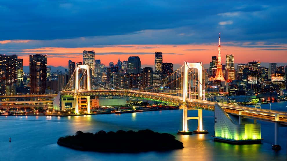 Rainbow Bridge 桌布 壁紙 — 彩虹橋在黃昏時分在東京灣上空閃耀，東京塔在火紅橙色和深藍色的天空下亮起。